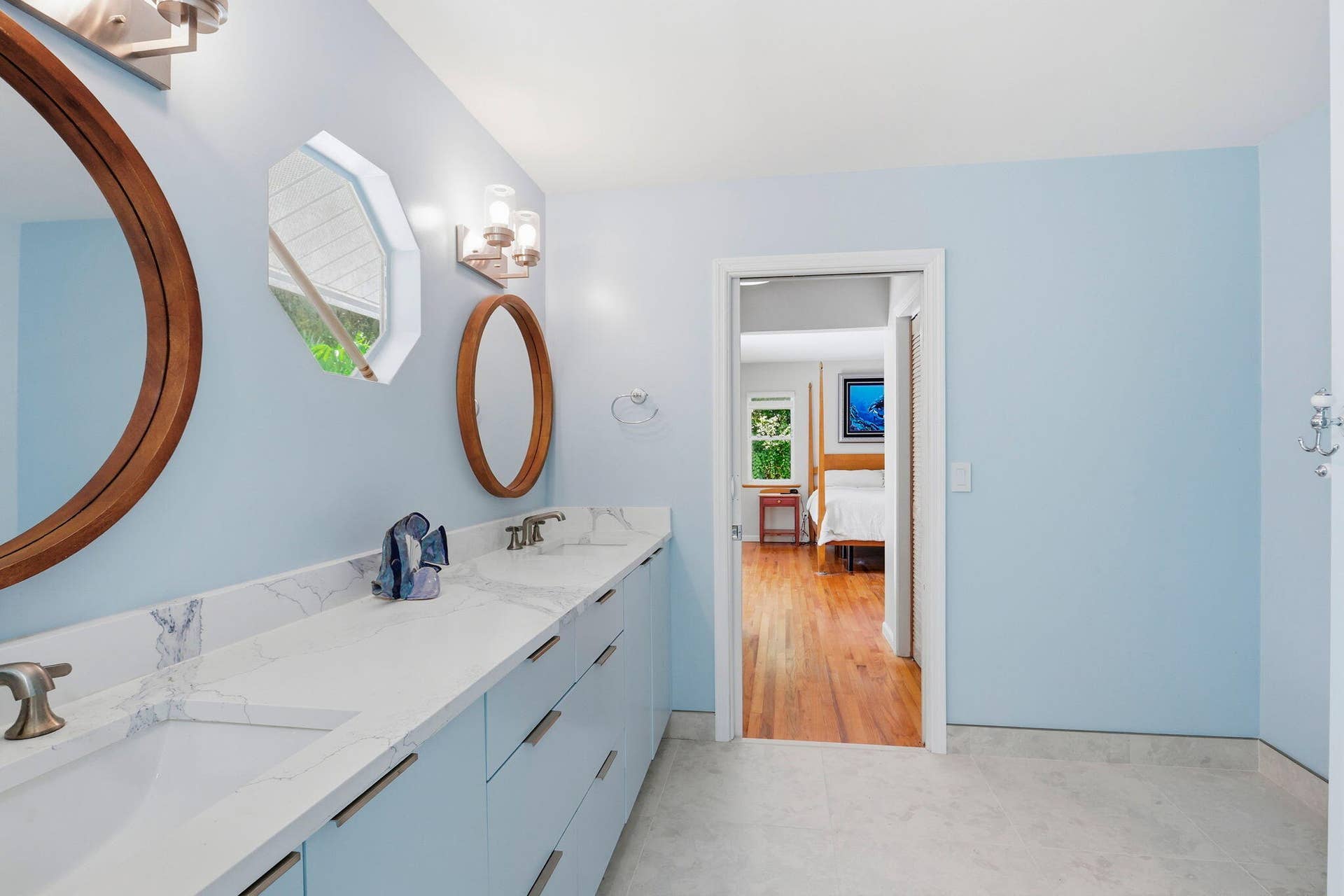 Dual vanity with integrated sinks and white countertops, light blue cabinetry, and a circular wooden-framed mirror