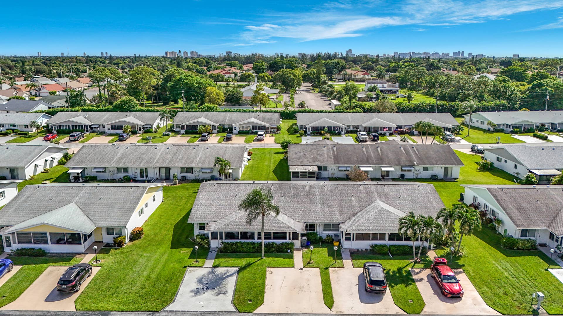 Well-manicured green spaces, mature palm trees, residential community setting, distant cityscape