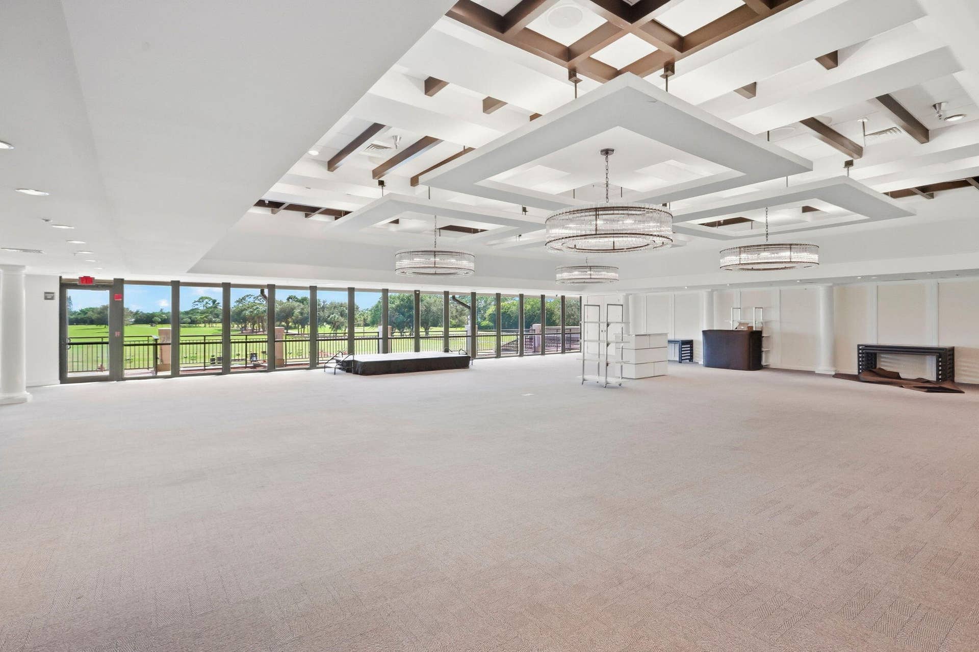 900 Greensward Lane, #209-G, Delray Beach, FL 33445 Expansive carpeted room featuring a coffered ceiling with integrated lighting, multiple decorative chandeliers, and a full wall of glass doors opening to an outdoor area
