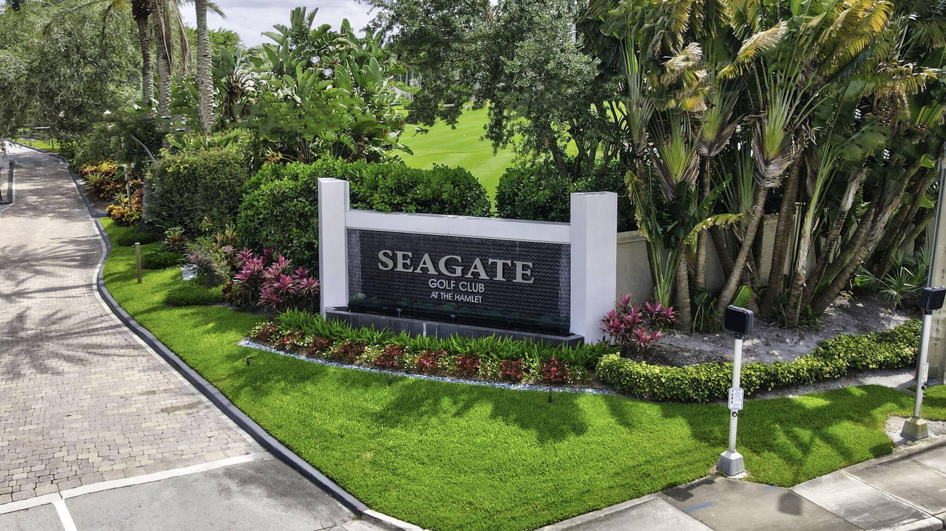 900 Greensward Lane, #209-G, Delray Beach, FL 33445 Entrance sign with a water feature, lush landscaping, mature trees, and manicured green spaces