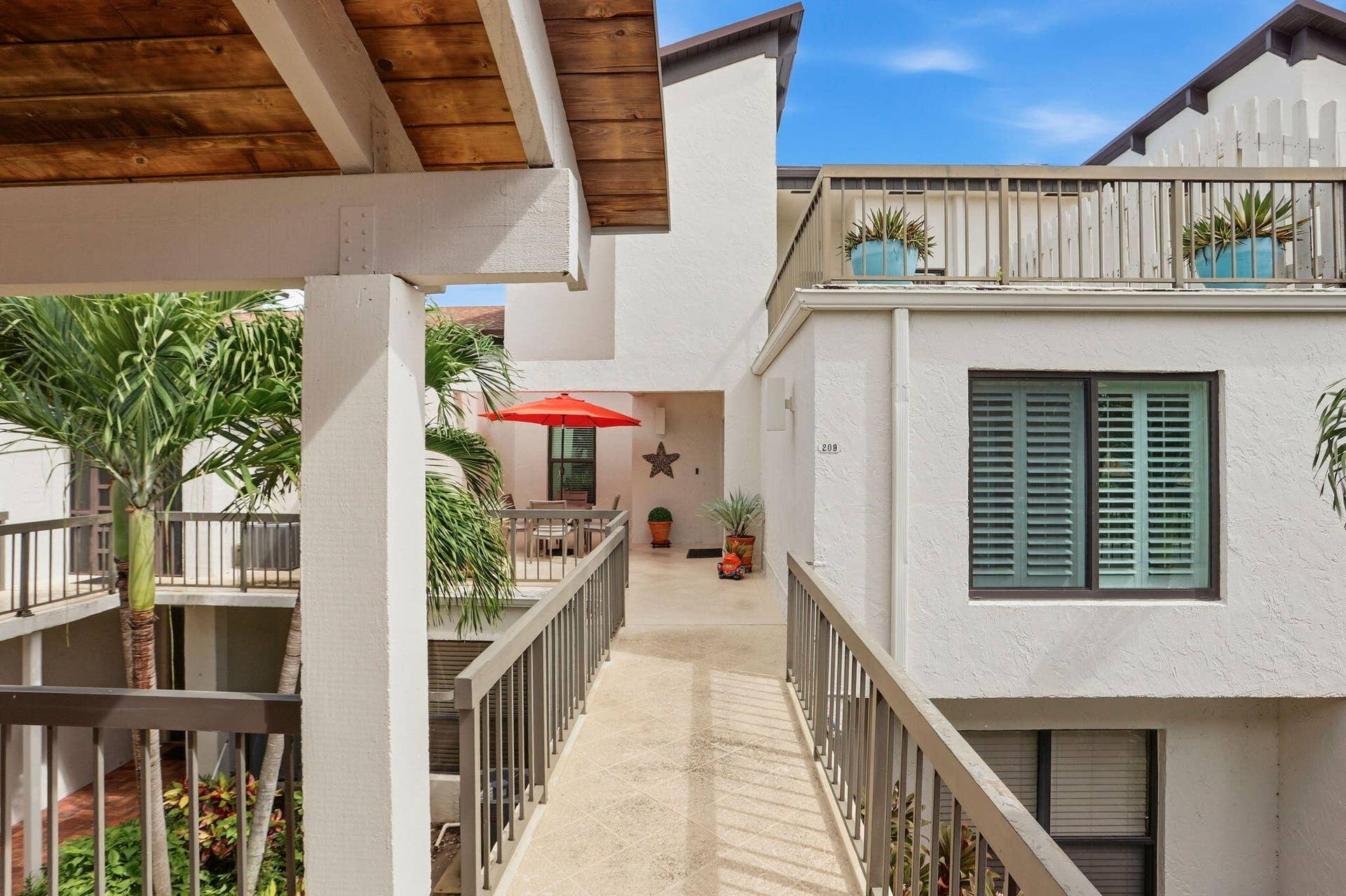 900 Greensward Lane, #209-G, Delray Beach, FL 33445 Exterior walkway with wood-finish ceiling, sturdy railings, and established palm trees