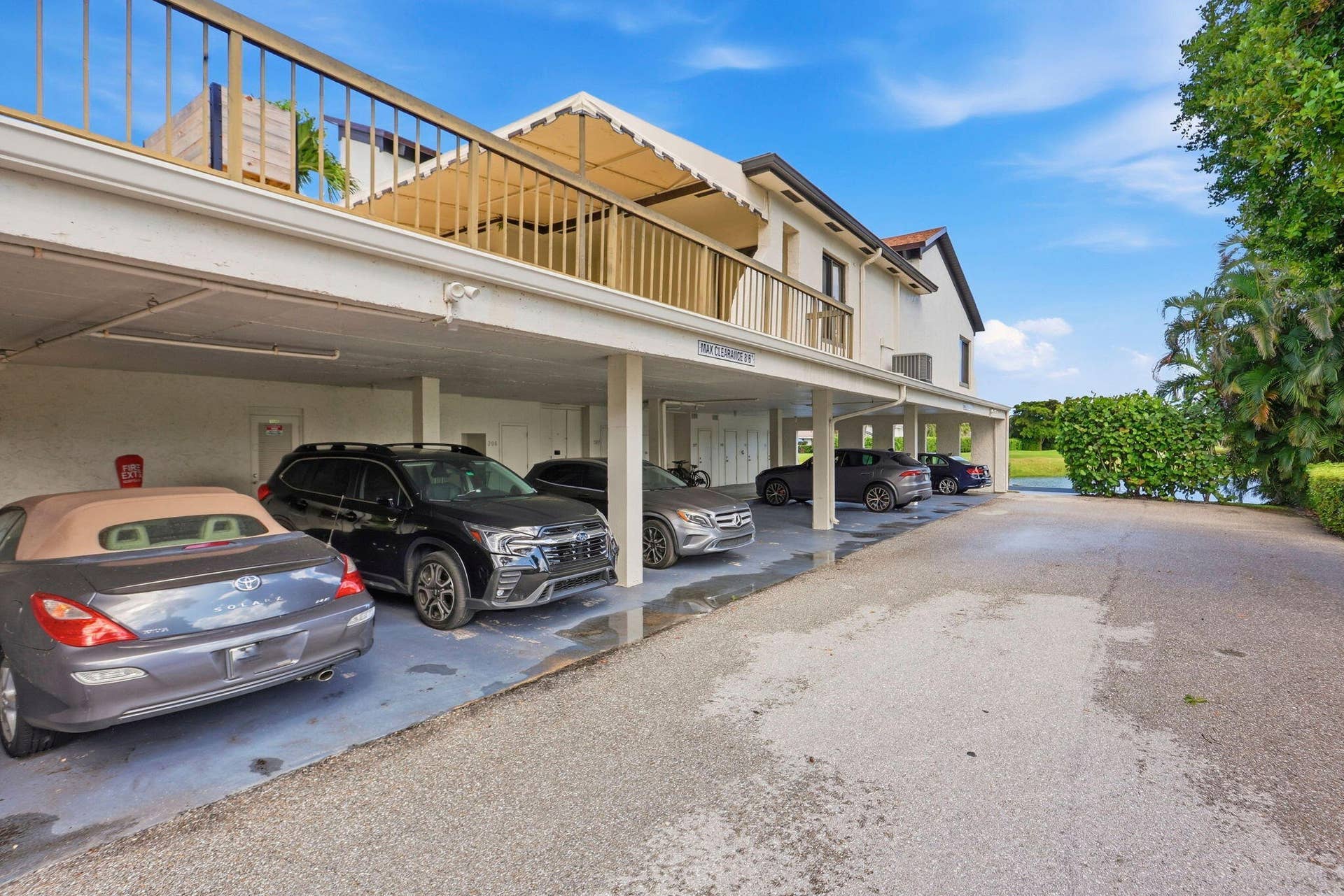 900 Greensward Lane, #209-G, Delray Beach, FL 33445 Covered parking garage with multiple spaces, featuring a second-story balcony with a canopy and a metal railing