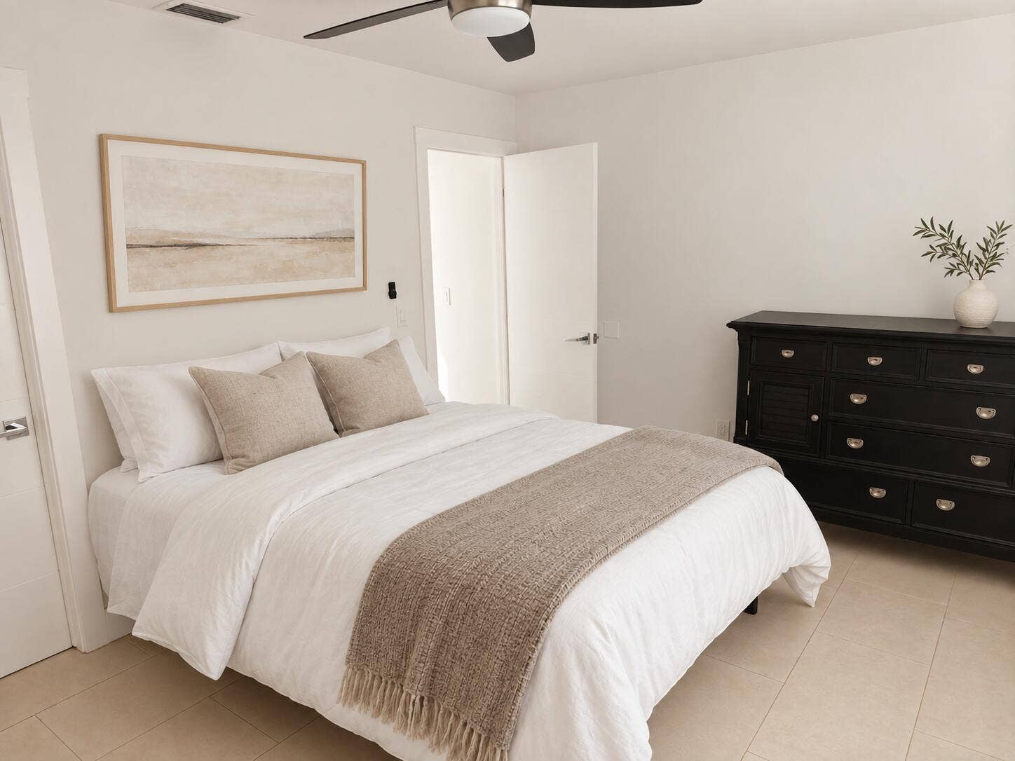 White walls with a contrasting black dresser, light-colored tile flooring, and a ceiling fan