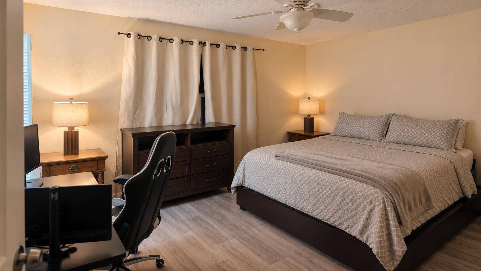 Light wood-finish flooring, ceiling fan with integrated lighting, and window with privacy curtains