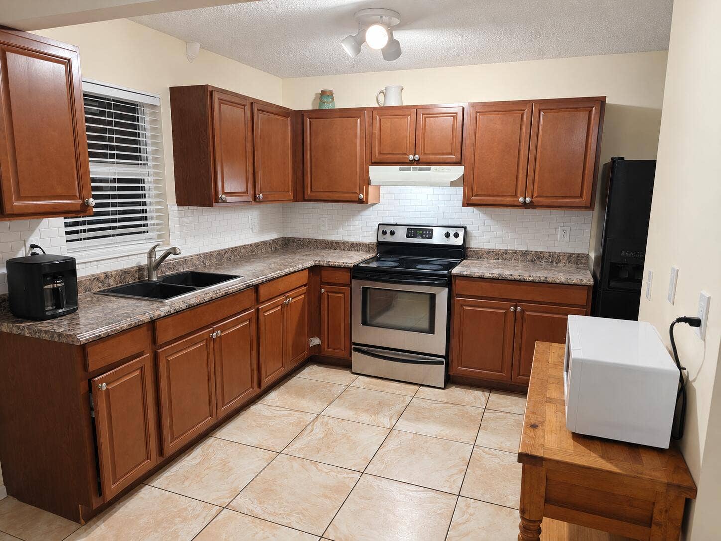 L-shaped kitchen featuring wood-finish cabinetry, a dual basin sink, stainless steel range, and tile flooring
