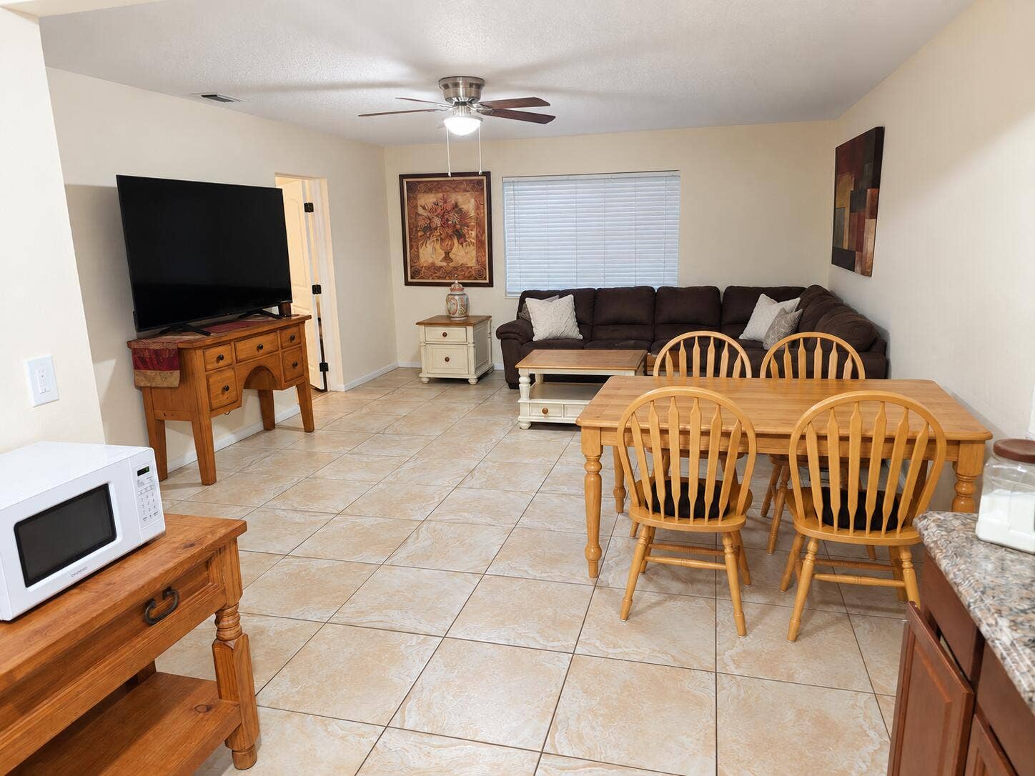 Neutral-toned ceramic tile flooring, ceiling fan with integrated lighting, and a large window with blinds