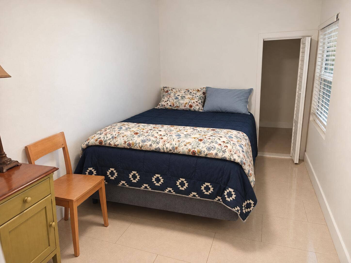 Smooth tile flooring, white walls, window with horizontal blinds, built-in closet with bifold doors