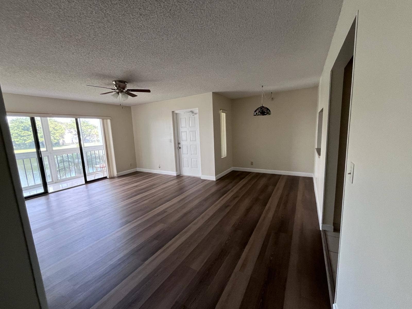 1002 Green Pine Boulevard, #F2, West Palm Beach, FL 33409 Spacious living area featuring wood-finish flooring, sliding glass doors to a balcony, and a ceiling fan
