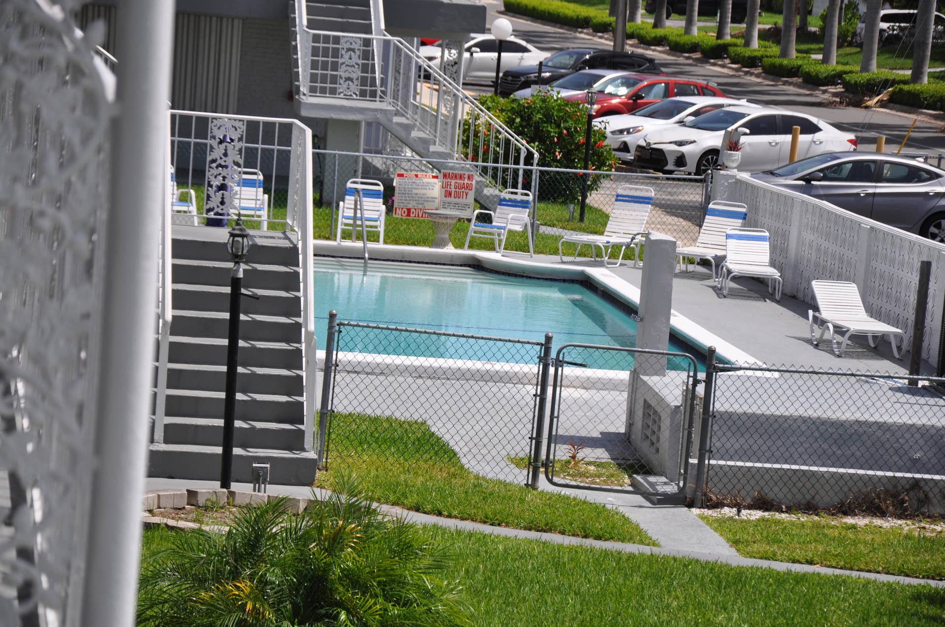 630 Layne Boulevard, #208, Hallandale Beach, Hallandale Beach, FL 33009 Community swimming pool with a surrounding chain-link fence, concrete deck, and adjacent green space