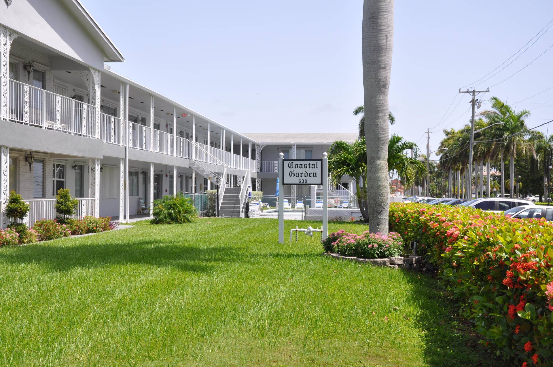 630 Layne Boulevard, #208, Hallandale Beach, Hallandale Beach, FL 33009 Manicured lawn with mature landscaping, a two-story building featuring white railing balconies, and exterior staircases