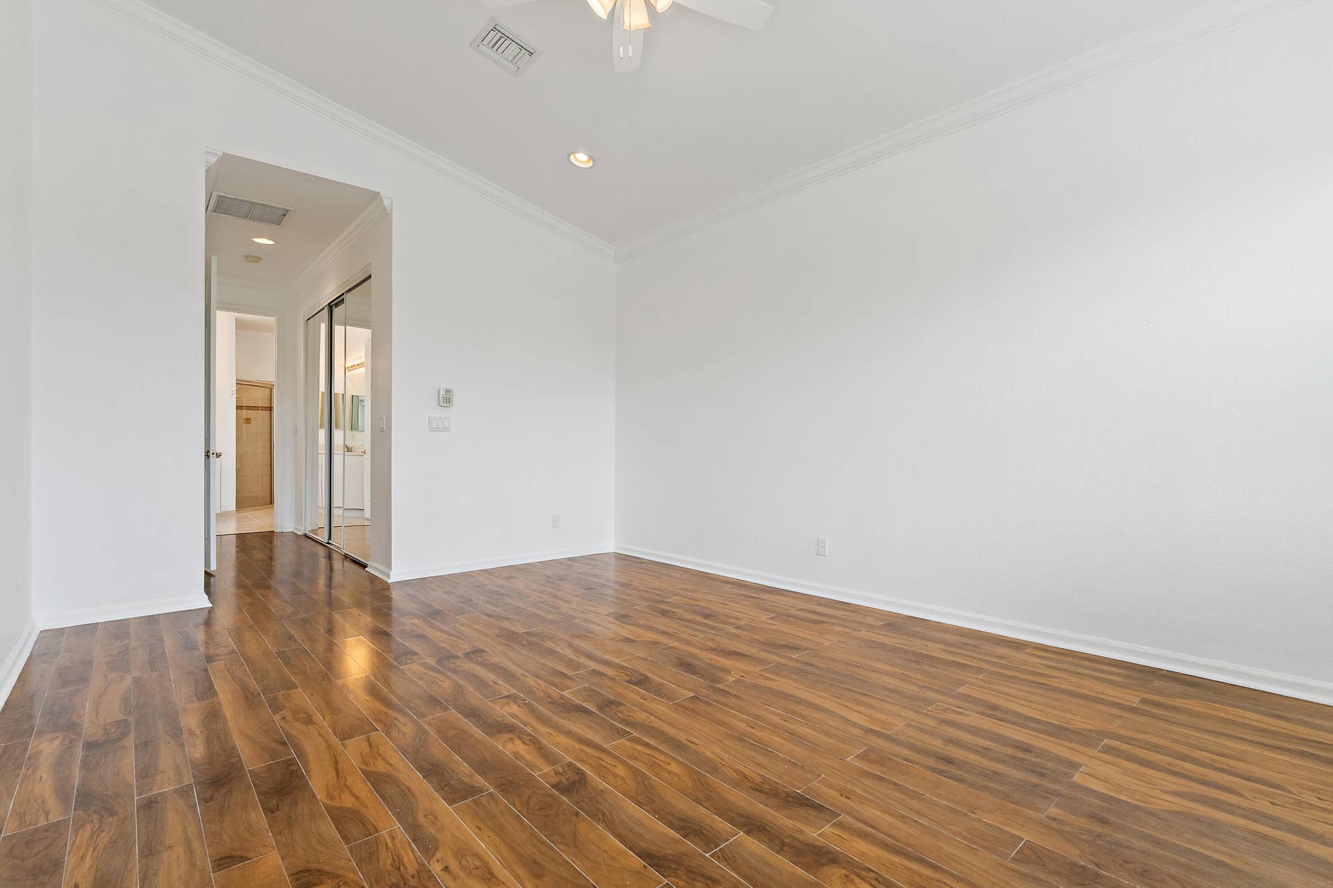 5183 SE Graham Drive, Stuart, FL 34997 The primary bedroom has plenty of room for a king bed and sitting area, with wood-look floors, crown molding, and a ceiling fan. A short hallway leads to the walk-in closet and private bath, giving the suite a quiet, separate feel.