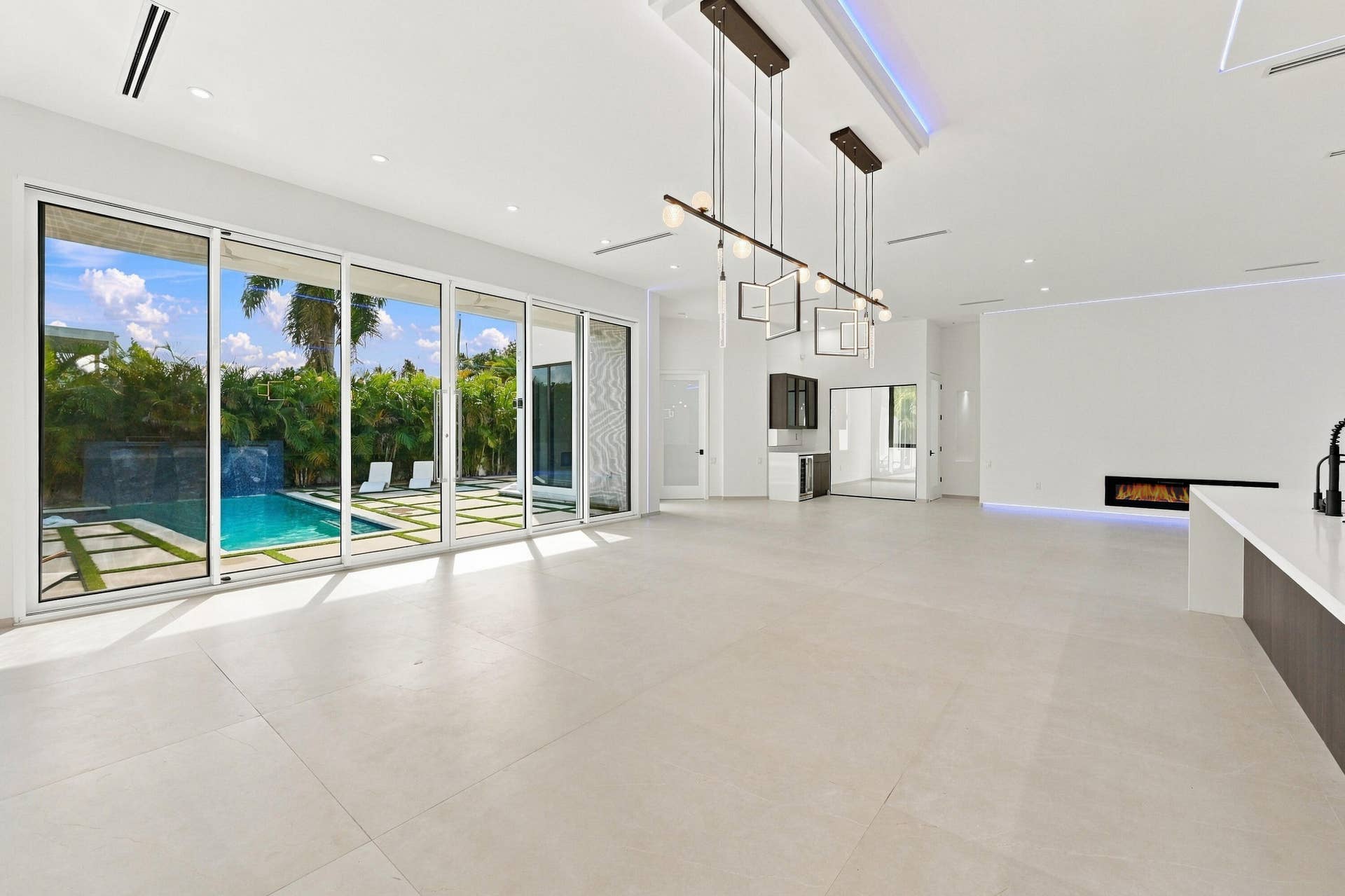 Expansive sliding glass doors, contemporary linear fireplace, recessed lighting, sleek kitchen island, and a custom built-in bar