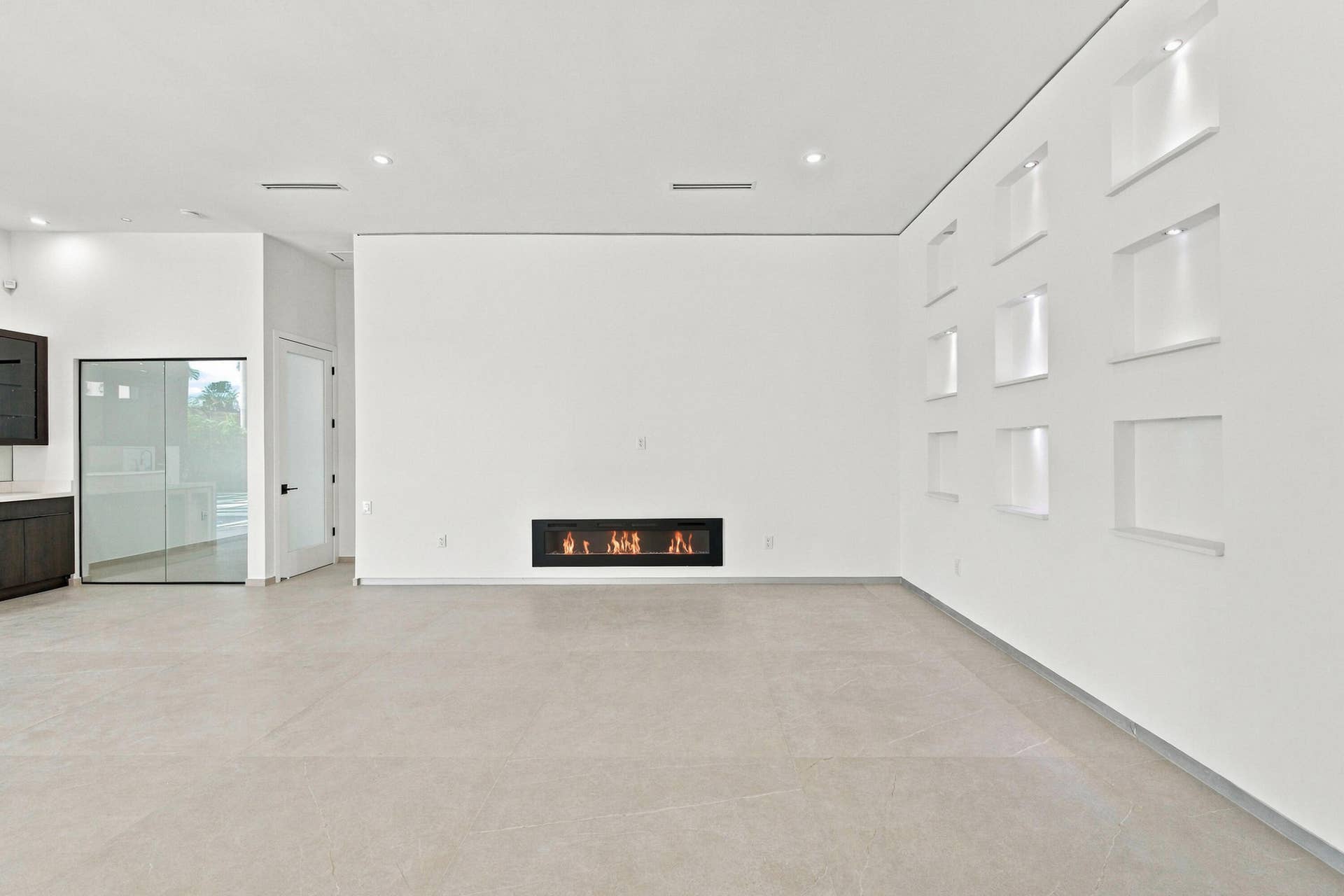 Built-in linear fireplace, recessed wall niches with accent lighting, dark wood-finish cabinetry, light-toned flooring, and recessed ceiling lighting