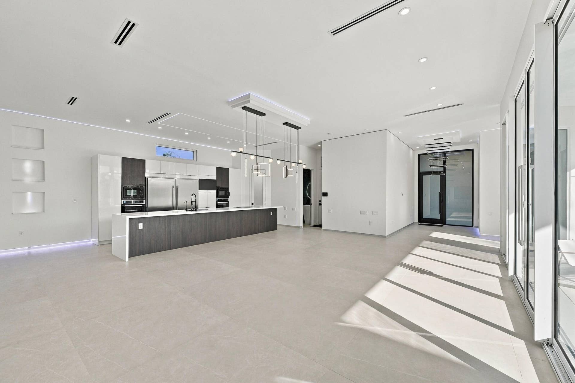 Modern open-concept living space featuring polished concrete flooring, recessed ceiling lighting, and expansive glass sliding doors flooding the area with natural light