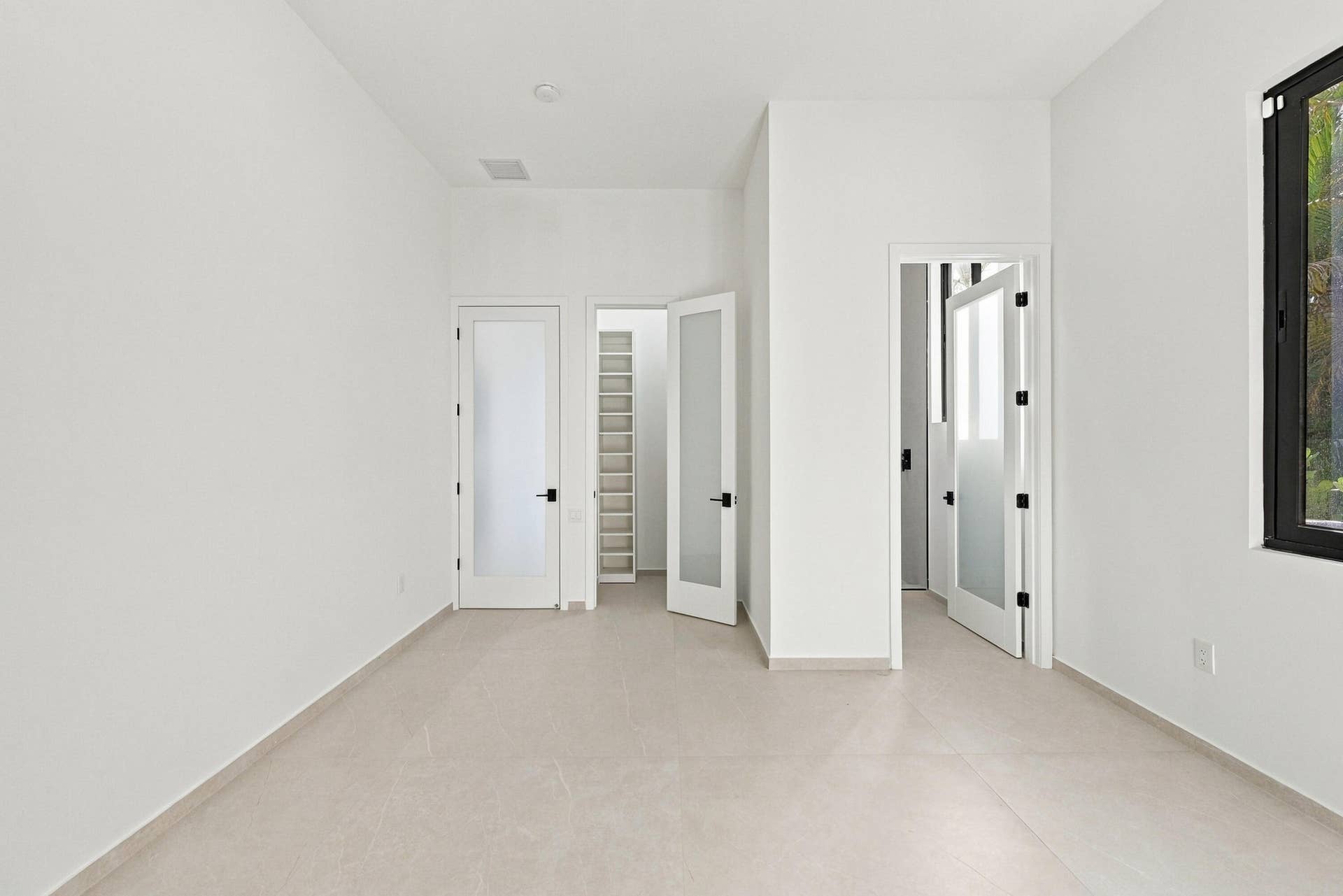 Bright, open interior featuring multiple white panel doors with black hardware, neutral flooring throughout, and clean white walls with recessed ceiling details