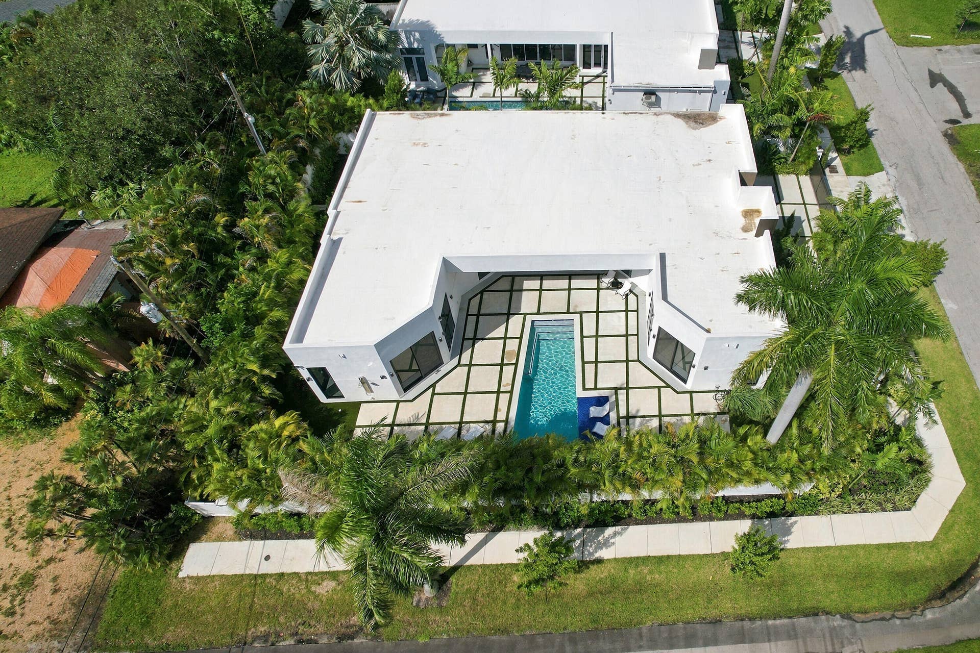 Aerial view showcasing a modern residence with a striking screened pool enclosure featuring black framing, surrounded by mature landscaping and lush greenery