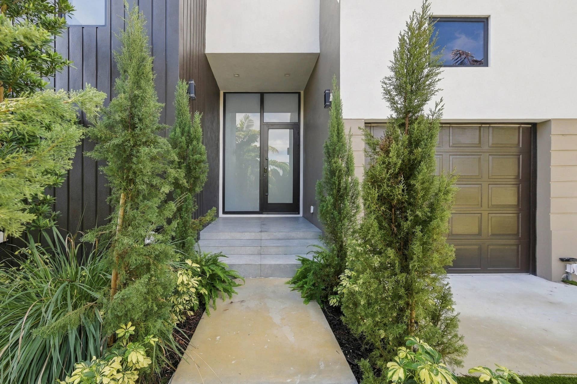 Modern exterior featuring black vertical siding, a white stucco finish, a paneled garage door, a glass entry door, and concrete steps