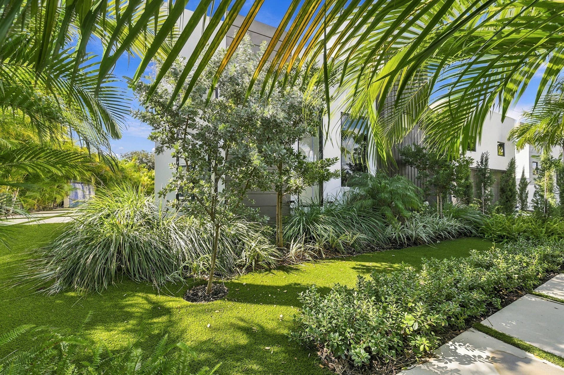 Lush tropical landscaping with mature palm trees, manicured lawn, and established shrub borders frames this serene outdoor setting