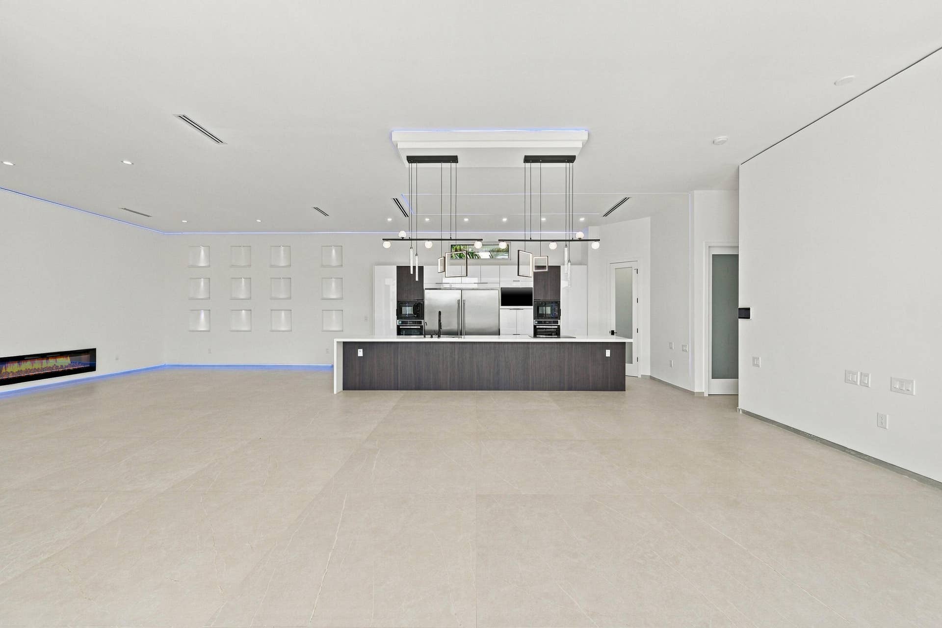 Expansive open-concept space featuring light wood-finish flooring, recessed ceiling lighting, and a contemporary dark-finished bar counter with integrated appliances