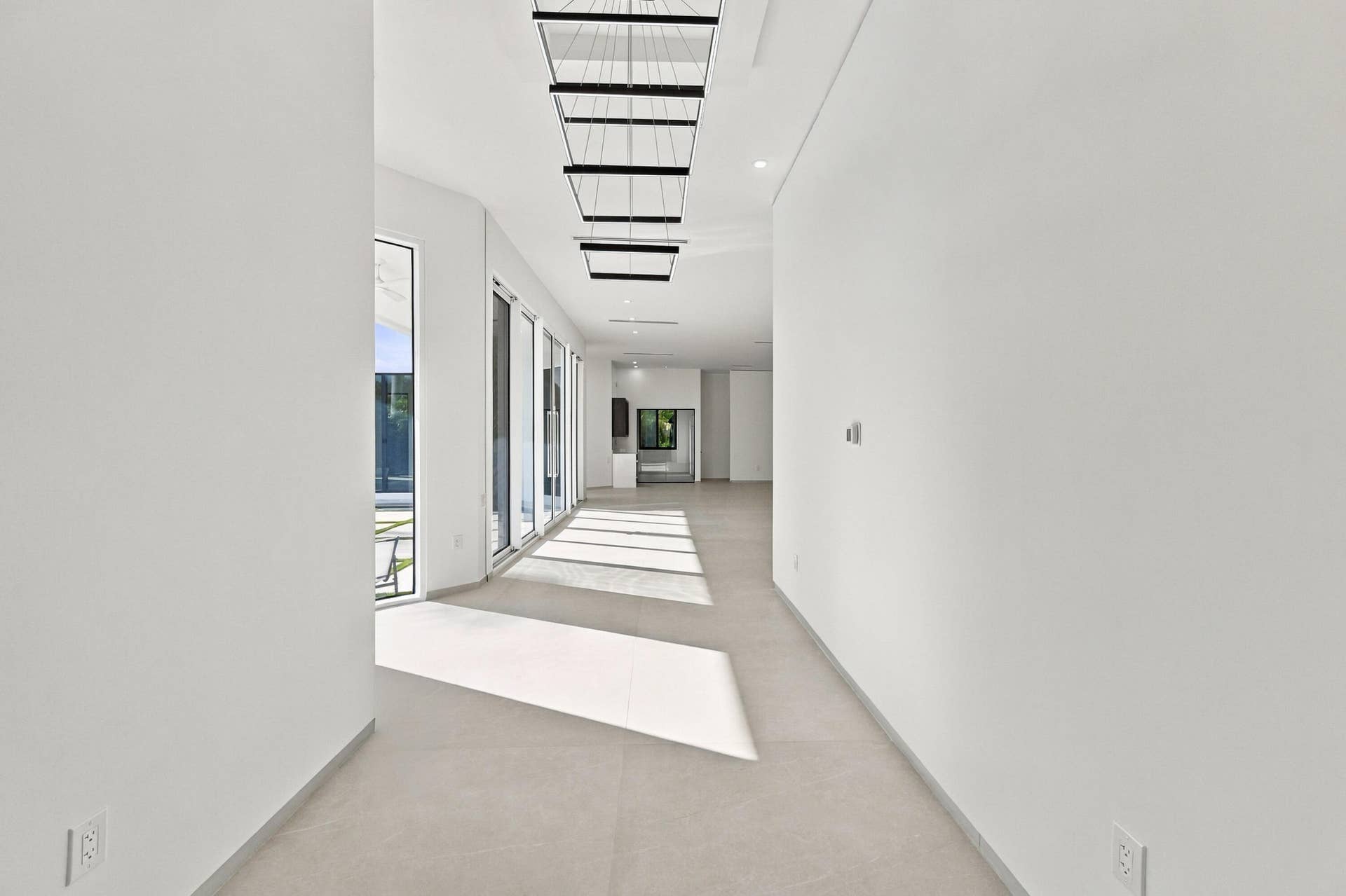 Expansive hallway featuring floor-to-ceiling glass doors, large format tile flooring, contemporary linear chandeliers, and recessed lighting