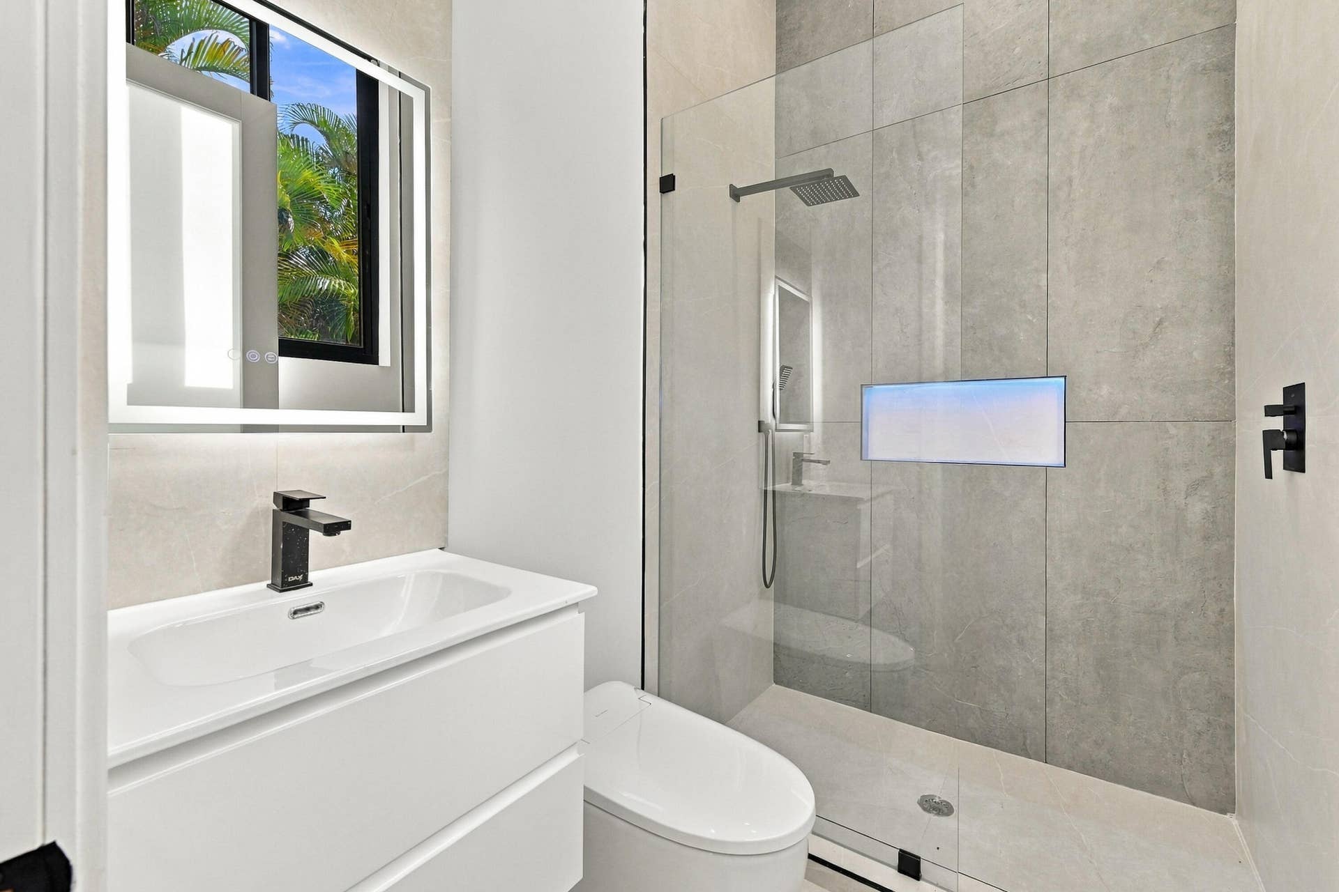 Floating vanity with integrated sink, backlit mirror, matte black fixtures, walk-in shower with glass enclosure, and wall-mounted rain shower head