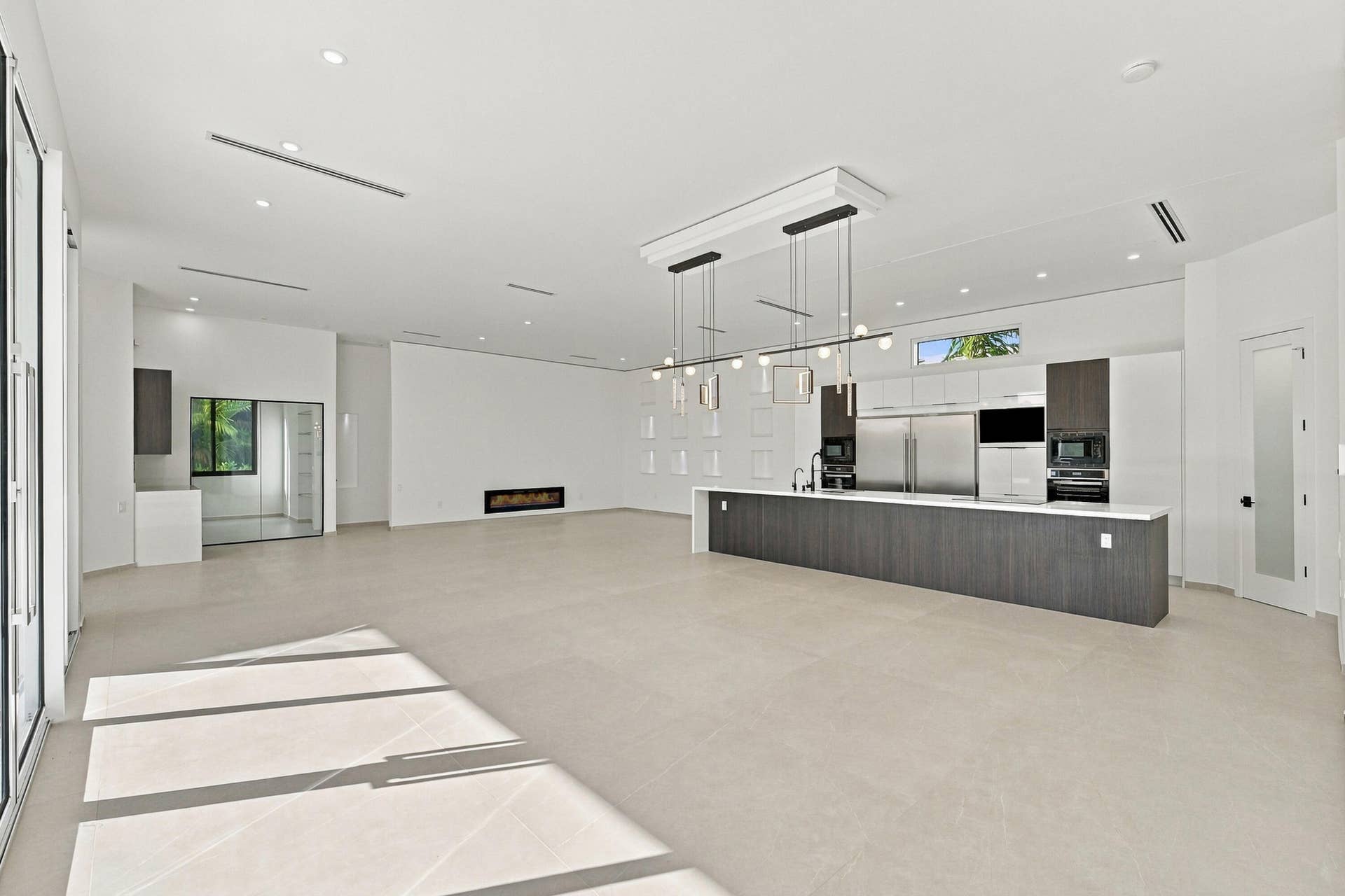 Spacious open-concept living area featuring polished concrete flooring, recessed and pendant lighting throughout, and a modern kitchen with dark cabinetry, stainless steel appliances, and a waterfall-edge island