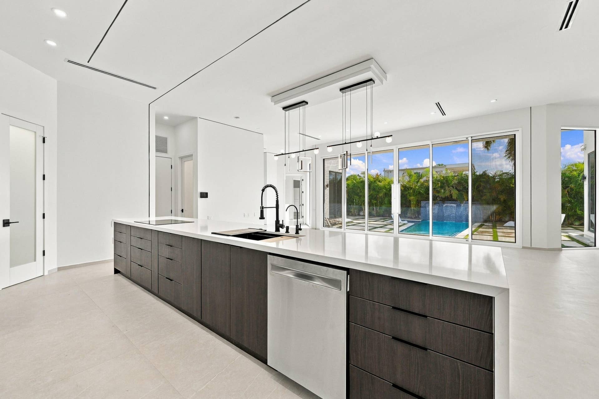 Chef's kitchen featuring a substantial island with wood-finish cabinetry, white quartz countertops, integrated dishwasher, and matte black faucet with pull-down spray