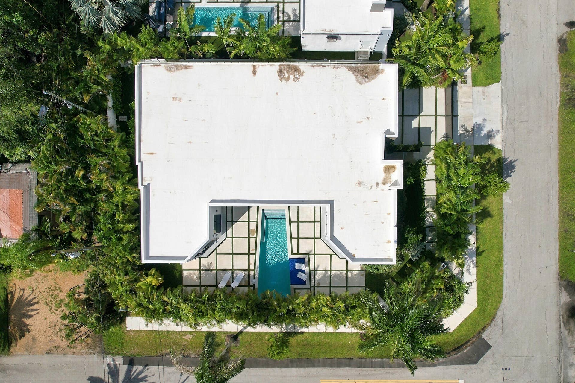 Aerial view showcasing a modern residence with a flat roof, clean white exterior, and a striking turquoise swimming pool surrounded by a dark-finished deck