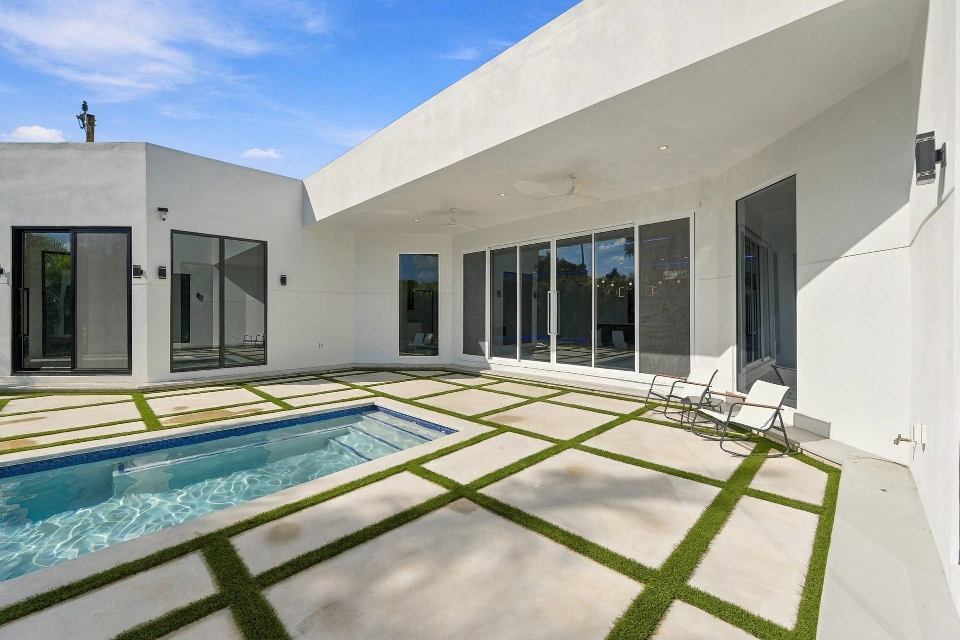 Modern exterior featuring an in-ground pool, expansive concrete patio with turf accents, and large sliding glass doors