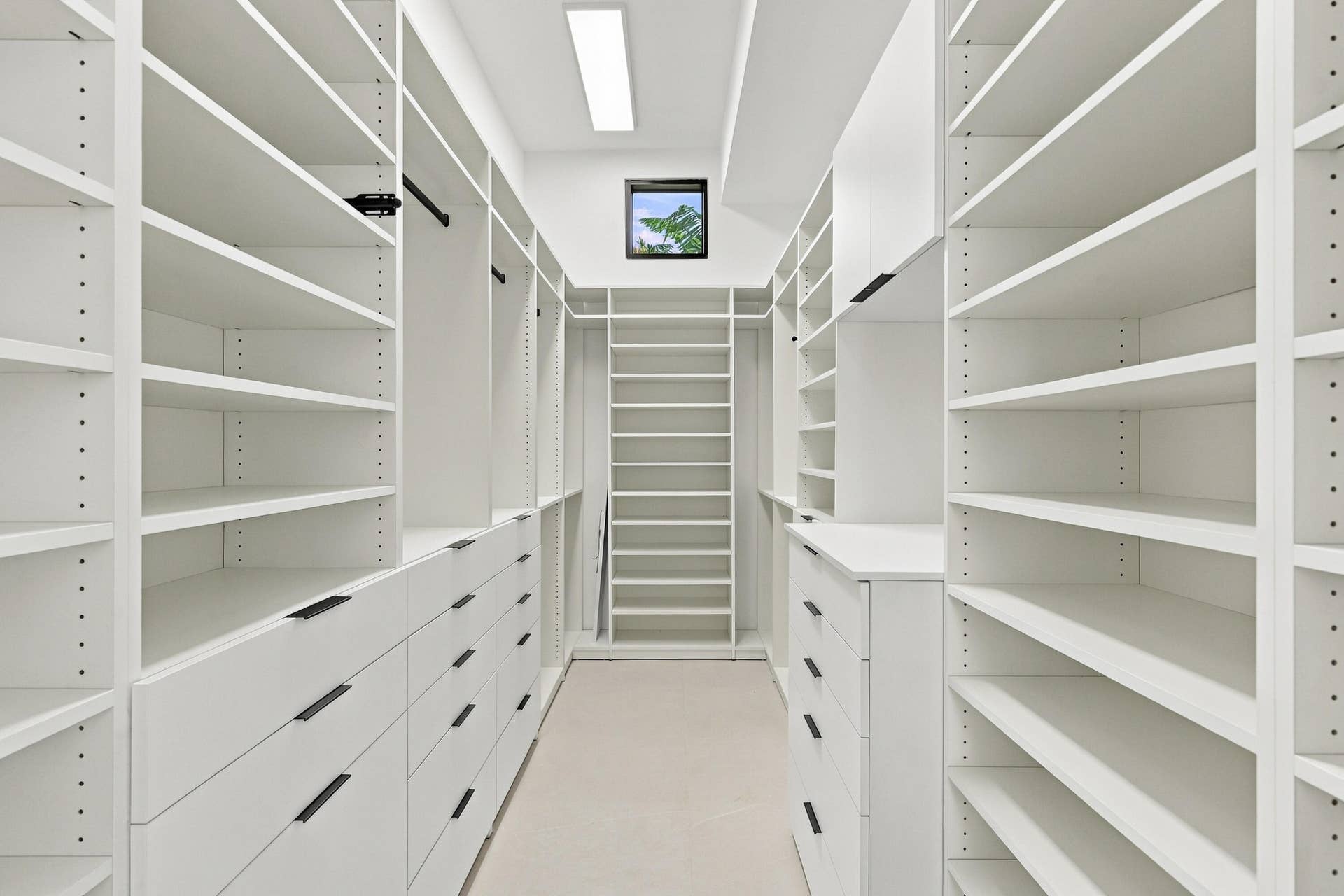 Custom closet system featuring extensive shelving, built-in drawers with modern hardware, integrated hanging rods, and a task ladder