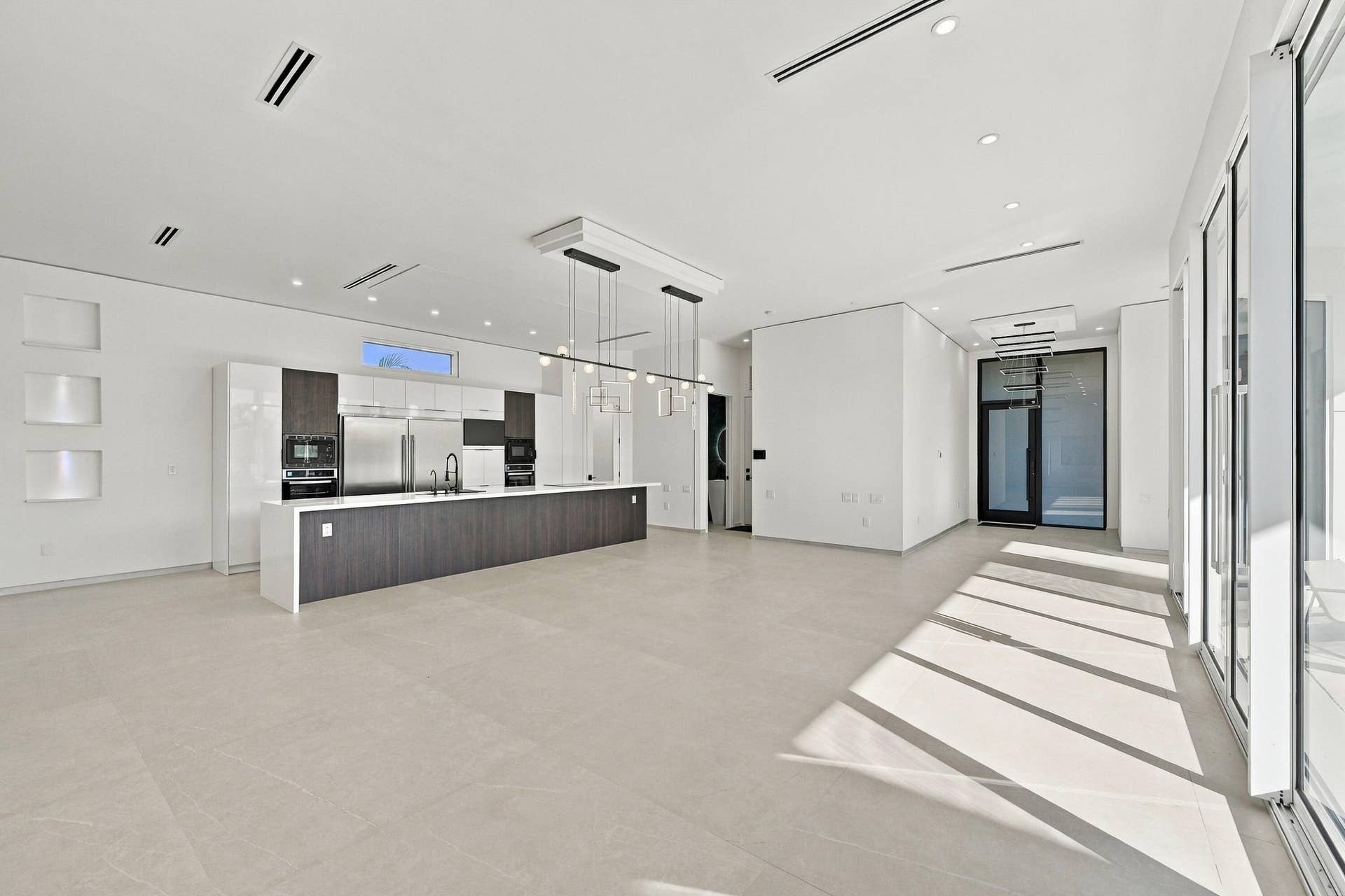 Spacious open-concept interior featuring light-toned flooring, a full-height glass door, and recessed lighting