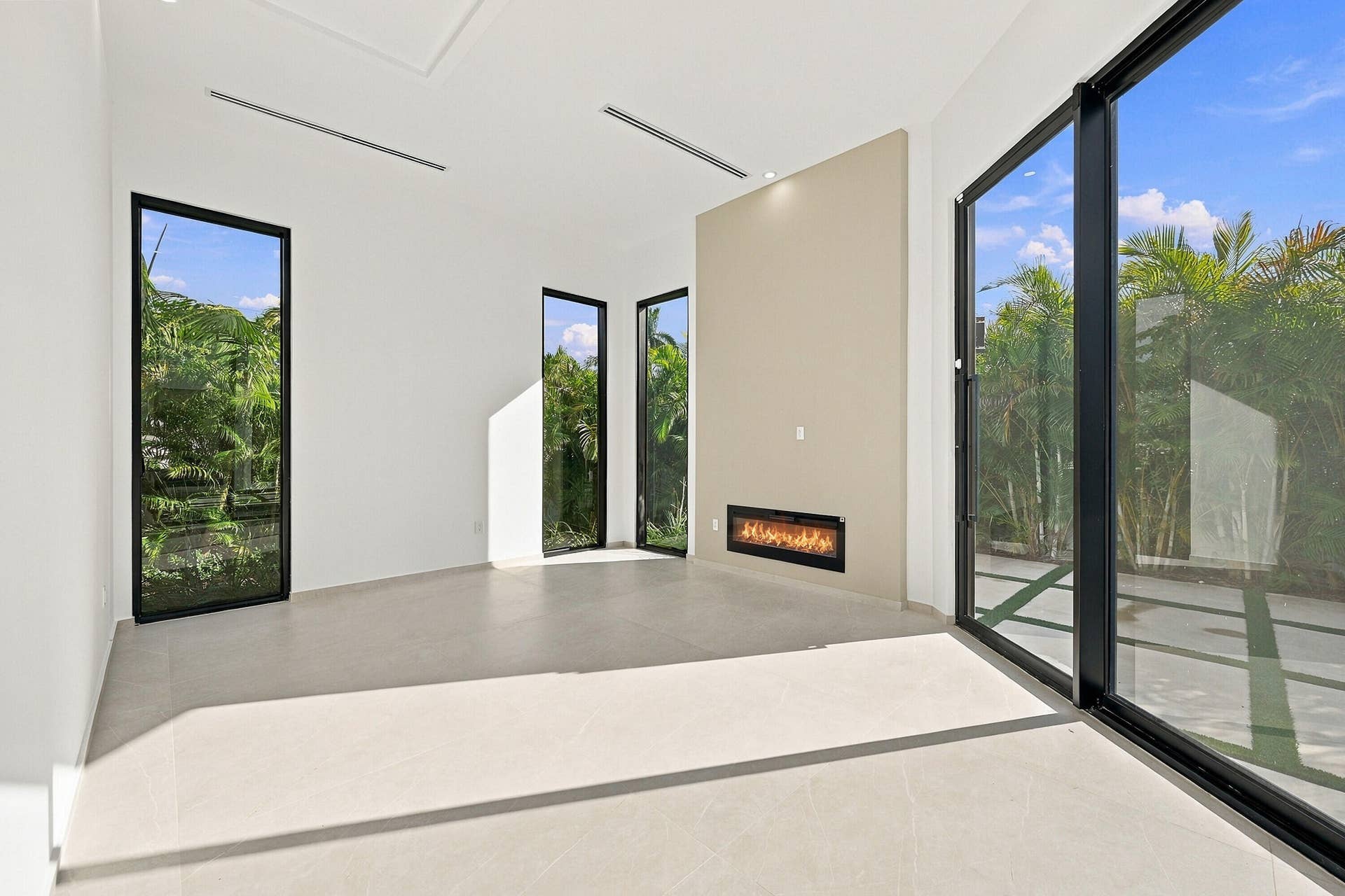 Modern living space featuring polished concrete flooring, floor-to-ceiling glass sliding doors with black metal framing, recessed ceiling lighting, and a striking linear fireplace insert