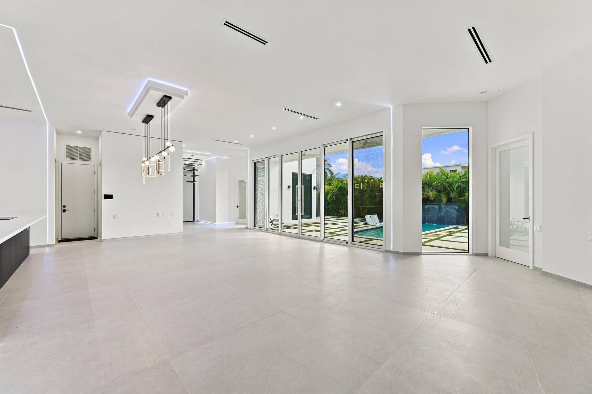 Expansive open-concept interior with polished concrete flooring, recessed ceiling lighting, and floor-to-ceiling glass sliding doors and windows framing landscaped grounds
