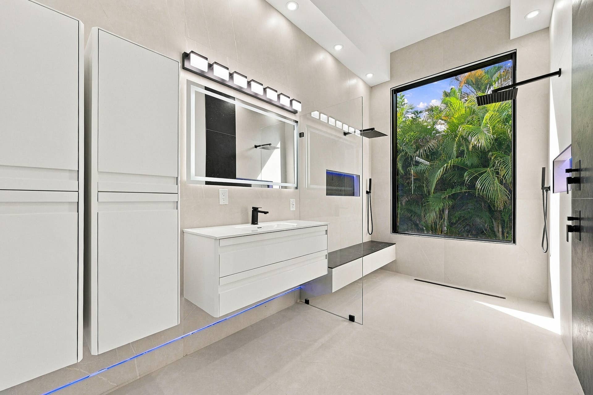 Spa-inspired primary bathroom featuring a floating white vanity with integrated sink, frameless glass shower enclosure, linear ceiling lighting, and large-scale nature artwork