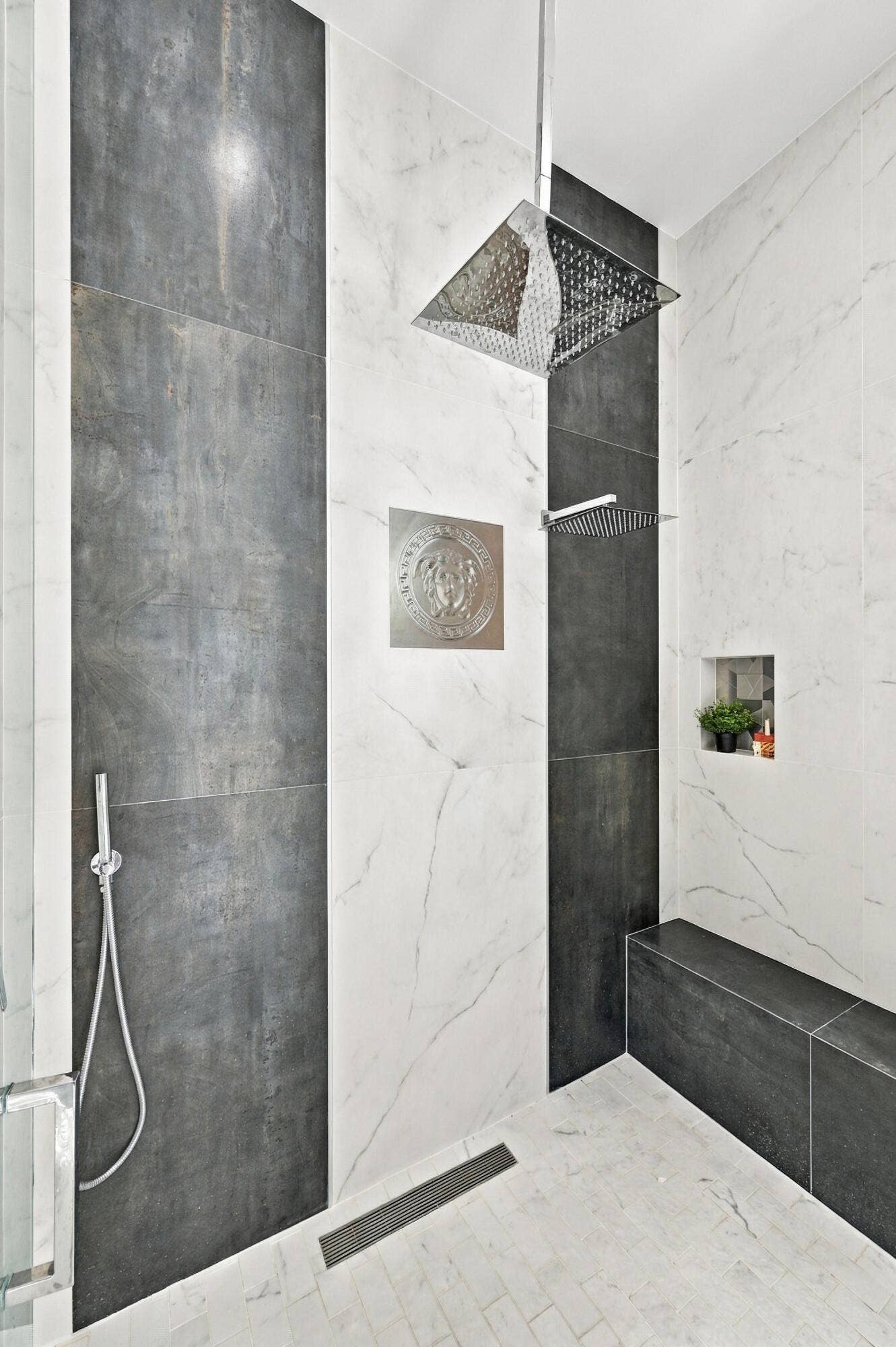 110 NE 16TH Place, Fort Lauderdale, FL 33305 Spa-inspired primary bathroom featuring polished marble-finish wall and floor tile, a frameless glass enclosure, overhead rainfall showerhead with integrated body jets, and recessed storage niche