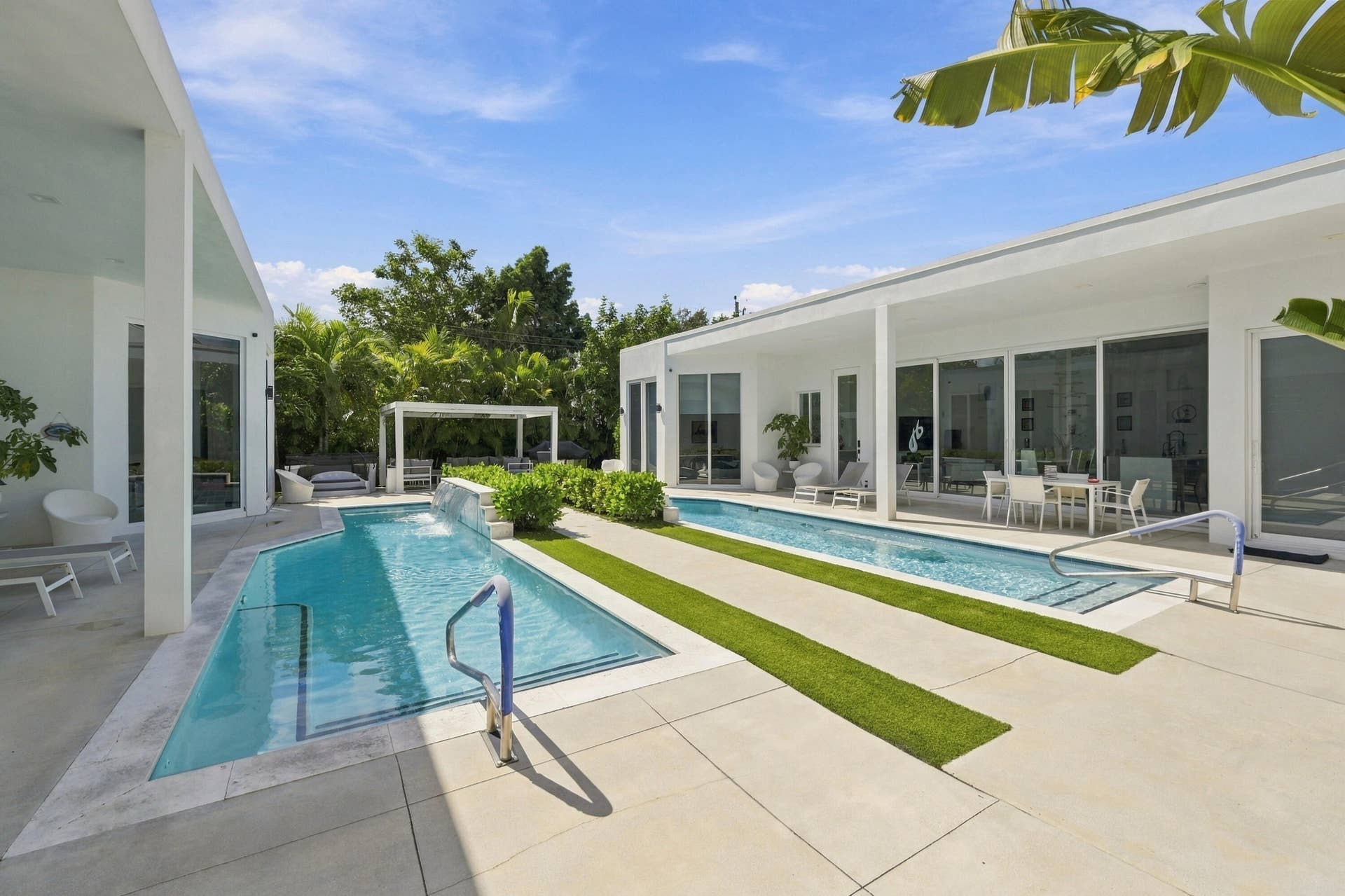110 NE 16TH Place, Fort Lauderdale, FL 33305 Expansive patio featuring two distinct pools, integrated turf strips, a white pergola, and extensive sliding glass doors