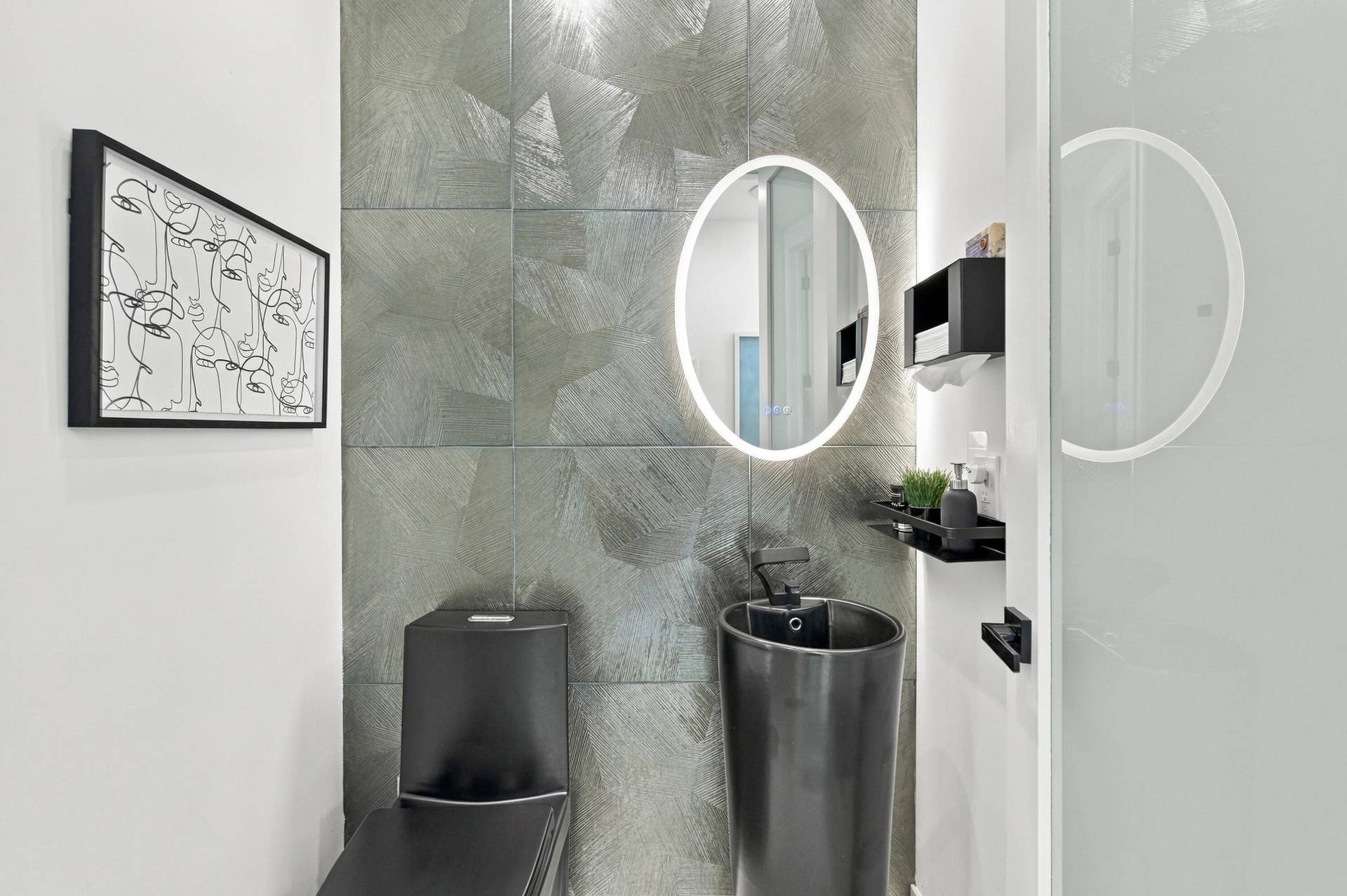 110 NE 16TH Place, Fort Lauderdale, FL 33305 Modern bathroom featuring dual illuminated oval mirrors with integrated LED lighting, gray tile wall treatment with geometric patterning, black cylindrical vessel sinks, and matte black wall-mounted fixtures