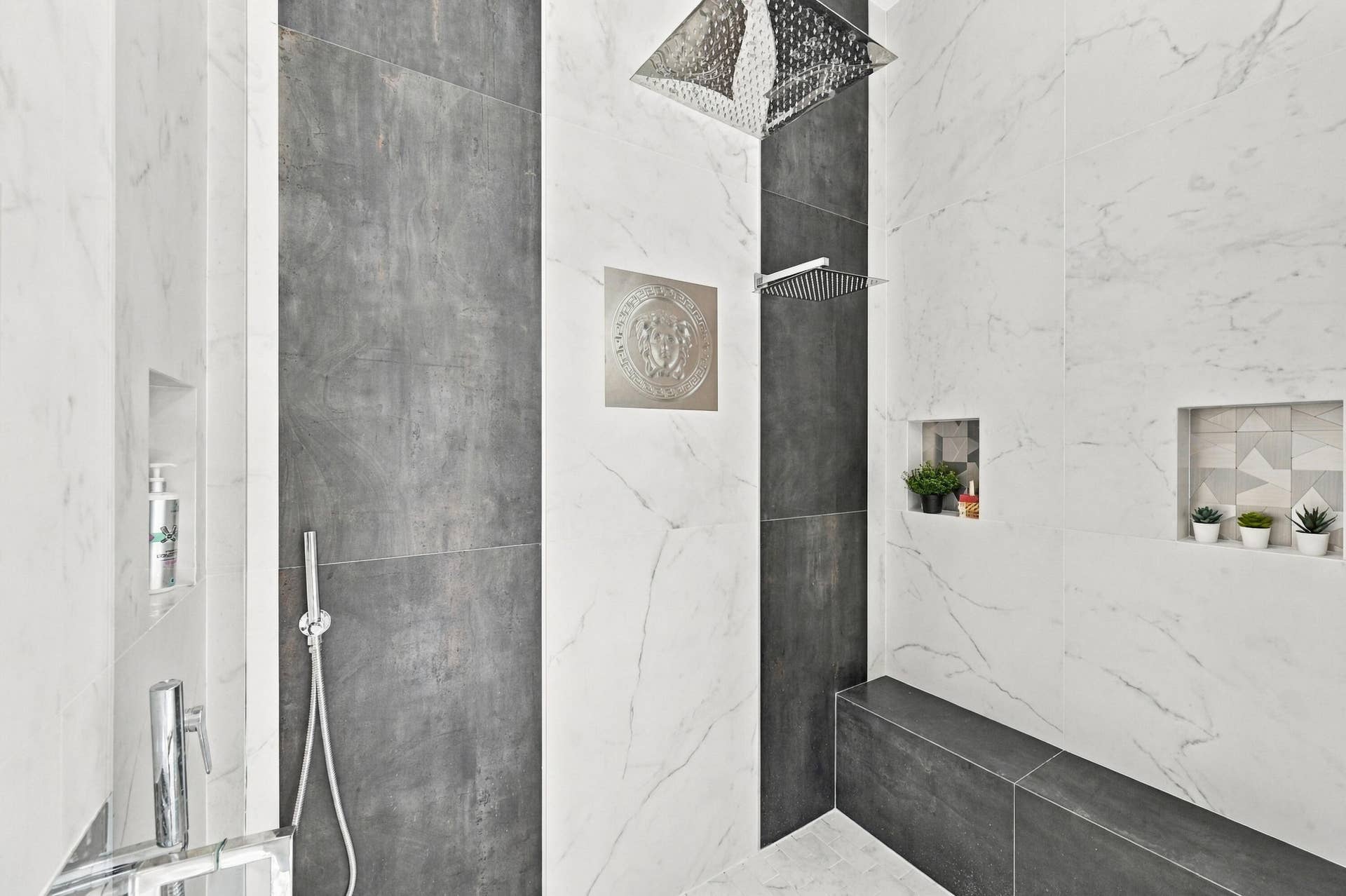 110 NE 16TH Place, Fort Lauderdale, FL 33305 White and gray tiled shower featuring a rainfall showerhead, handheld shower fixture, built-in shelving, and a tiled shower bench