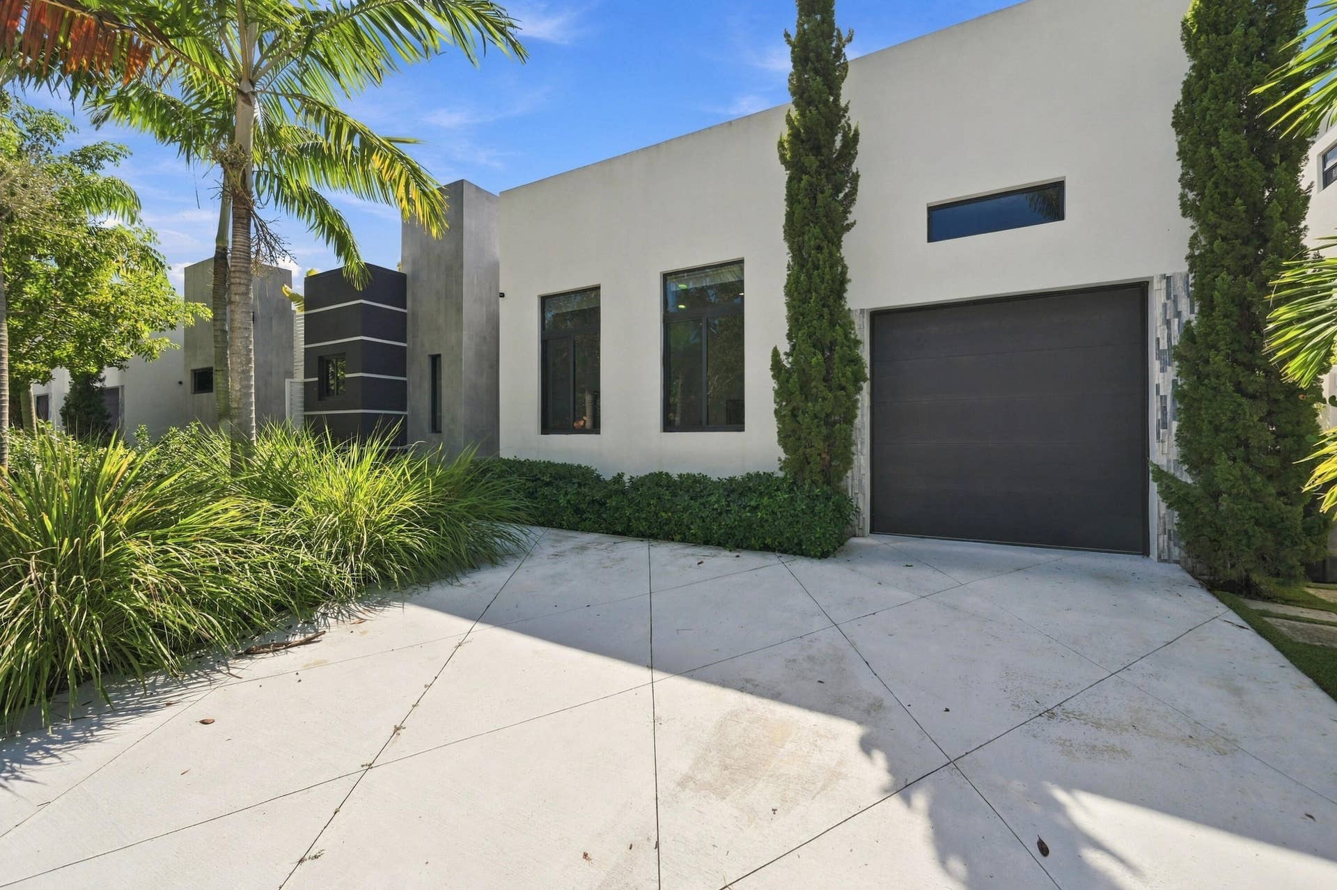110 NE 16TH Place, Fort Lauderdale, FL 33305 Modern exterior with a light stucco finish, featuring a dark garage door, multiple rectangular windows, and a paved driveway