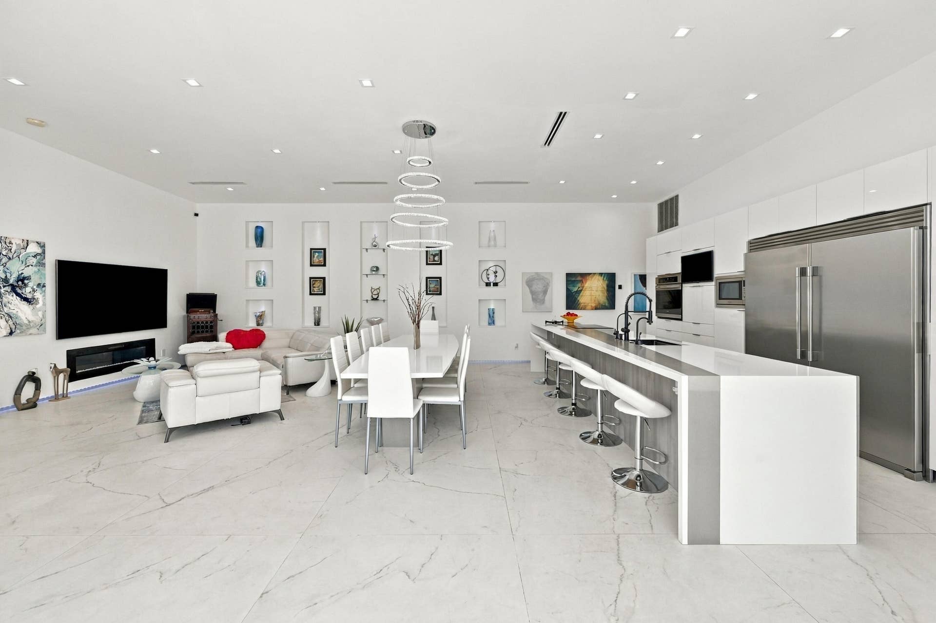 110 NE 16TH Place, Fort Lauderdale, FL 33305 Open-concept living and dining space featuring polished stone flooring, recessed ceiling lighting, and a modern kitchen with stainless steel appliances, white cabinetry, and waterfall-edge countertops