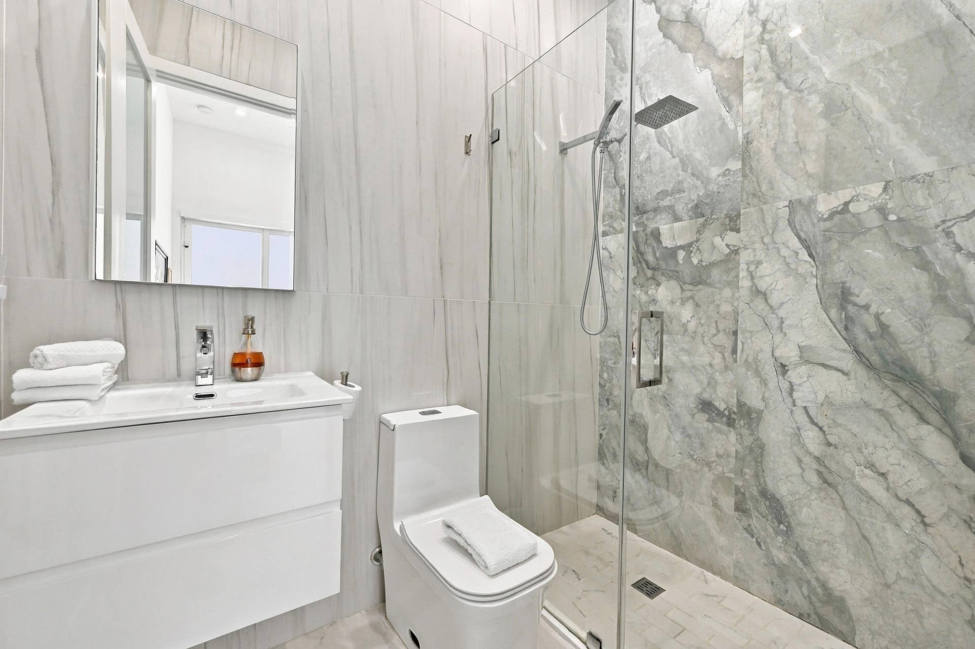 110 NE 16TH Place, Fort Lauderdale, FL 33305 Contemporary bathroom featuring a floating vanity with integrated sink, rectangular mirror, and a glass-enclosed shower with a rainfall showerhead