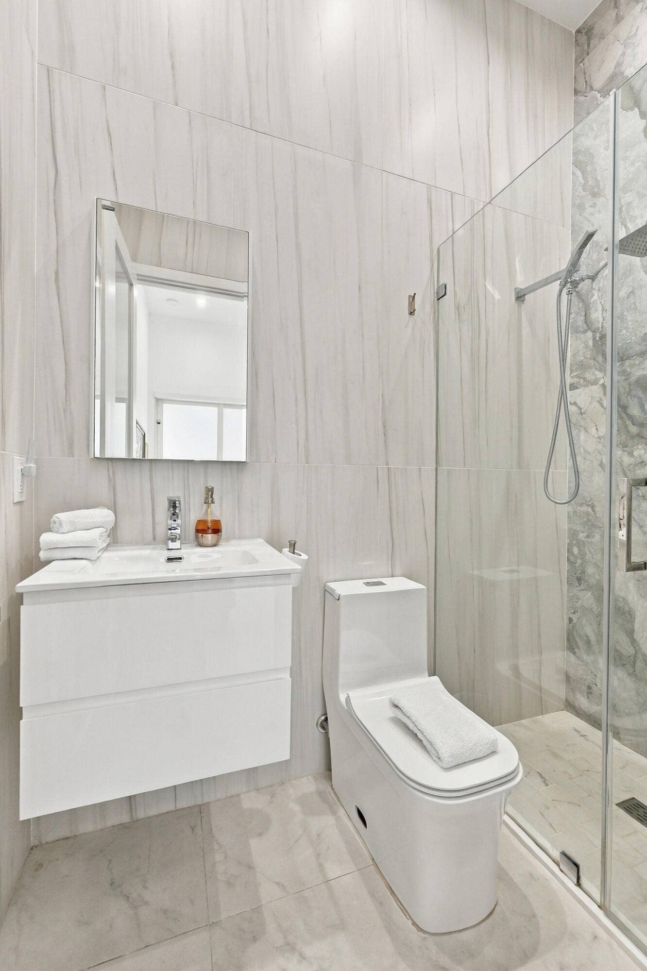 110 NE 16TH Place, Fort Lauderdale, FL 33305 Floating vanity with integrated sink, rectangular wall mirror, full-height tile shower enclosure, and white tile flooring