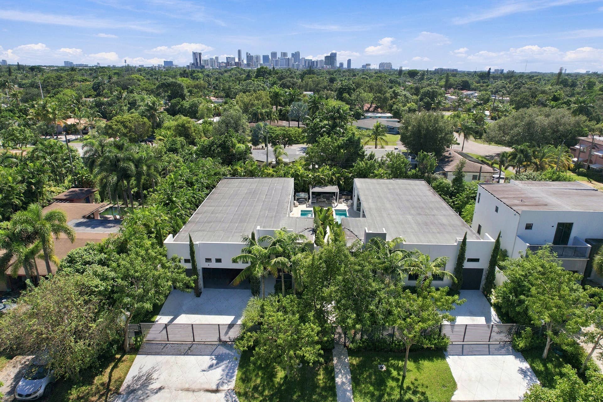110 NE 16TH Place, Fort Lauderdale, FL 33305 Modern architectural residence showcasing a flat-roof design with clean geometric lines, expansive covered outdoor entertaining spaces with integrated seating areas, mature landscaping throughout the grounds, and a lush tree-lined setting with cityscape visible in the distance