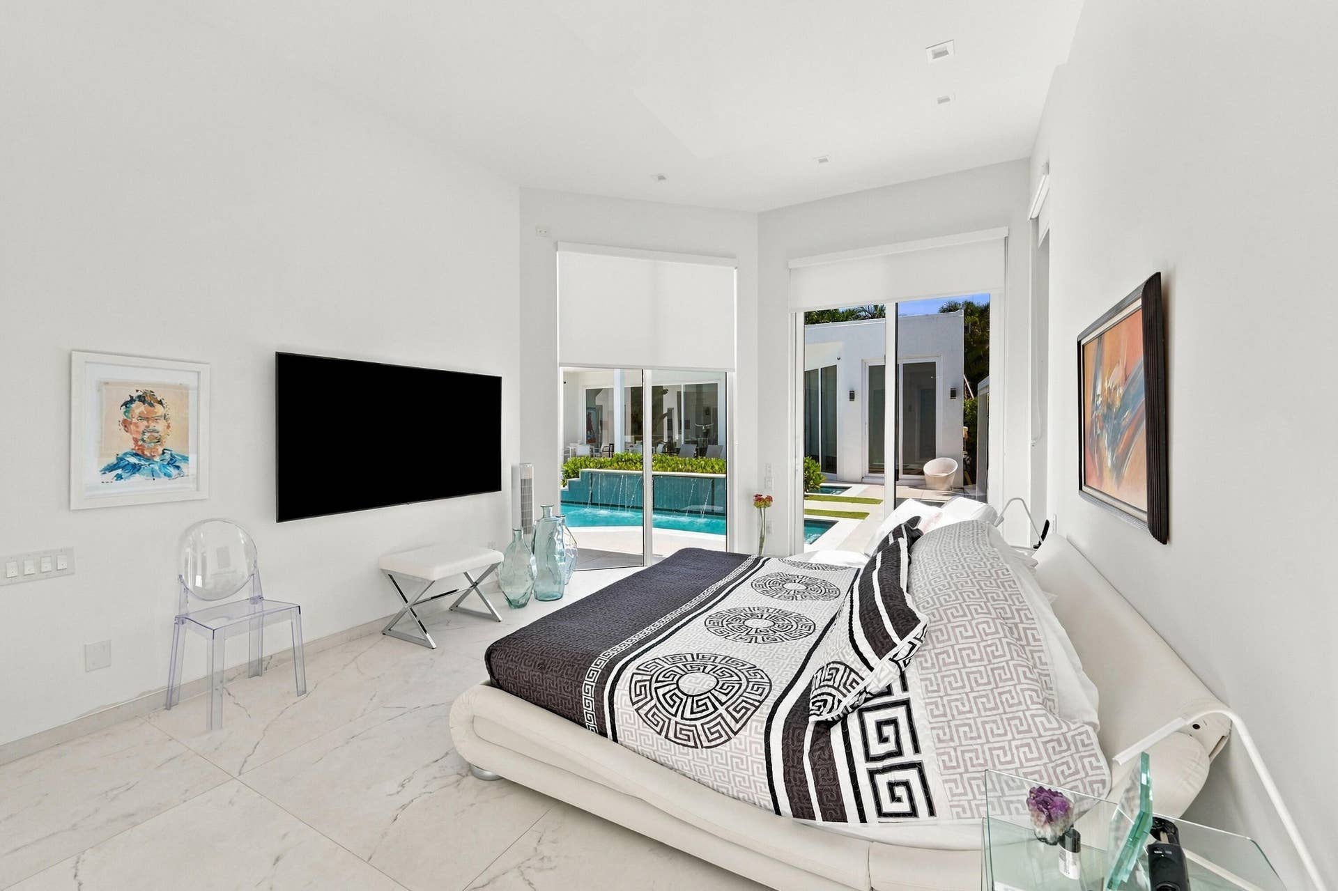 110 NE 16TH Place, Fort Lauderdale, FL 33305 Modern primary bedroom with floor-to-ceiling glass doors opening to exterior spaces, light-filled interiors with tile flooring, wall-mounted flat-screen television, and contemporary furnishings throughout