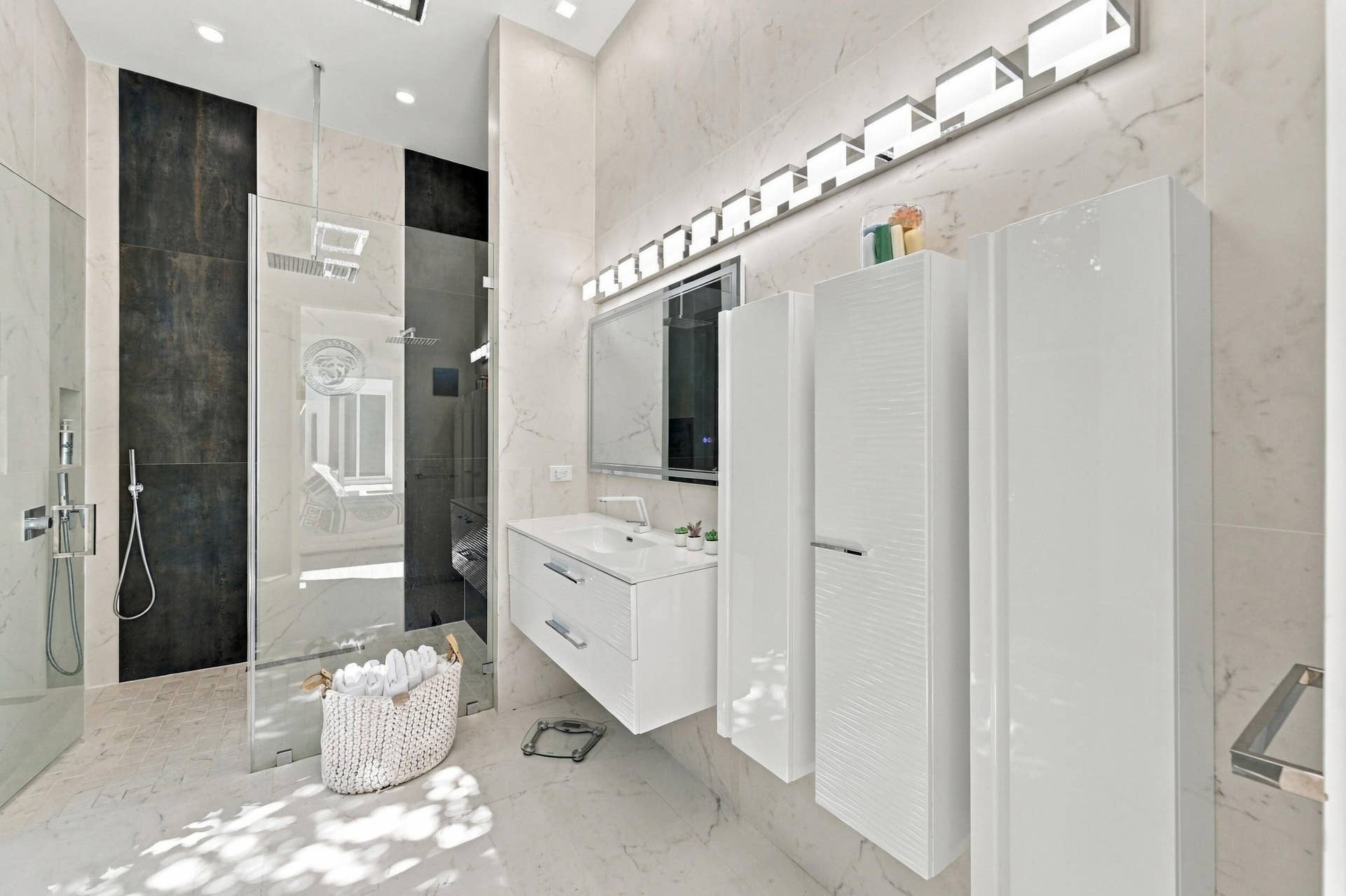 110 NE 16TH Place, Fort Lauderdale, FL 33305 Spa-inspired primary bathroom featuring a frameless glass-enclosed shower with black tile accent wall, floating white vanity with dual sinks and integrated storage, polished stone-finish flooring, linear LED vanity lighting, and recessed ceiling fixtures throughout