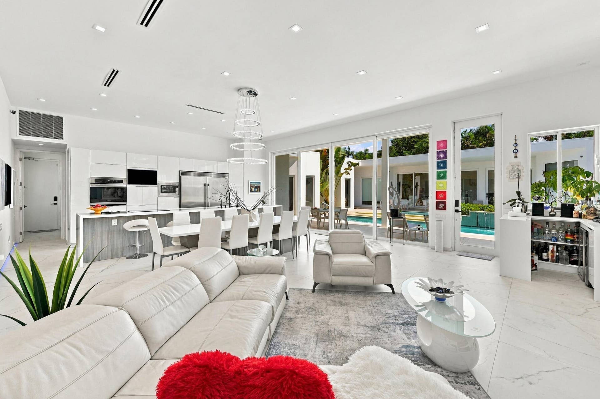 110 NE 16TH Place, Fort Lauderdale, FL 33305 Open-concept living space featuring polished stone flooring, expansive windows and glass sliding doors with natural light throughout, a modern kitchen with stainless steel appliances and white cabinetry, gray upholstered seating, recessed ceiling lighting, and a bright interior with multiple glass doors opening to outdoor spaces