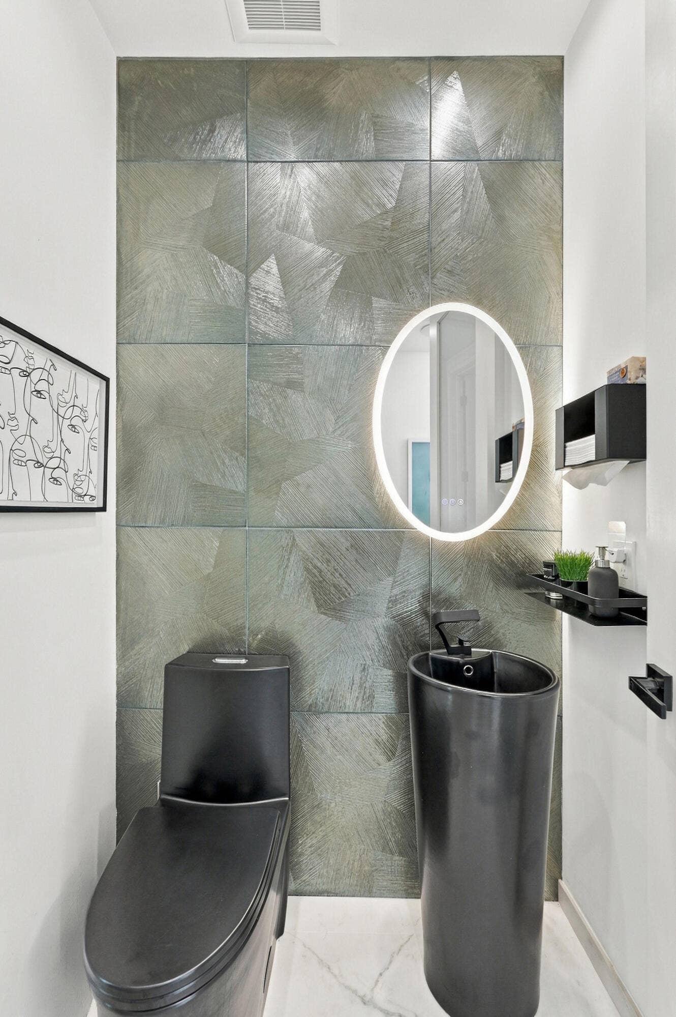 110 NE 16TH Place, Fort Lauderdale, FL 33305 Textured wall tiling, round illuminated vanity mirror, black pedestal sink, wall-mounted faucet, and black toilet