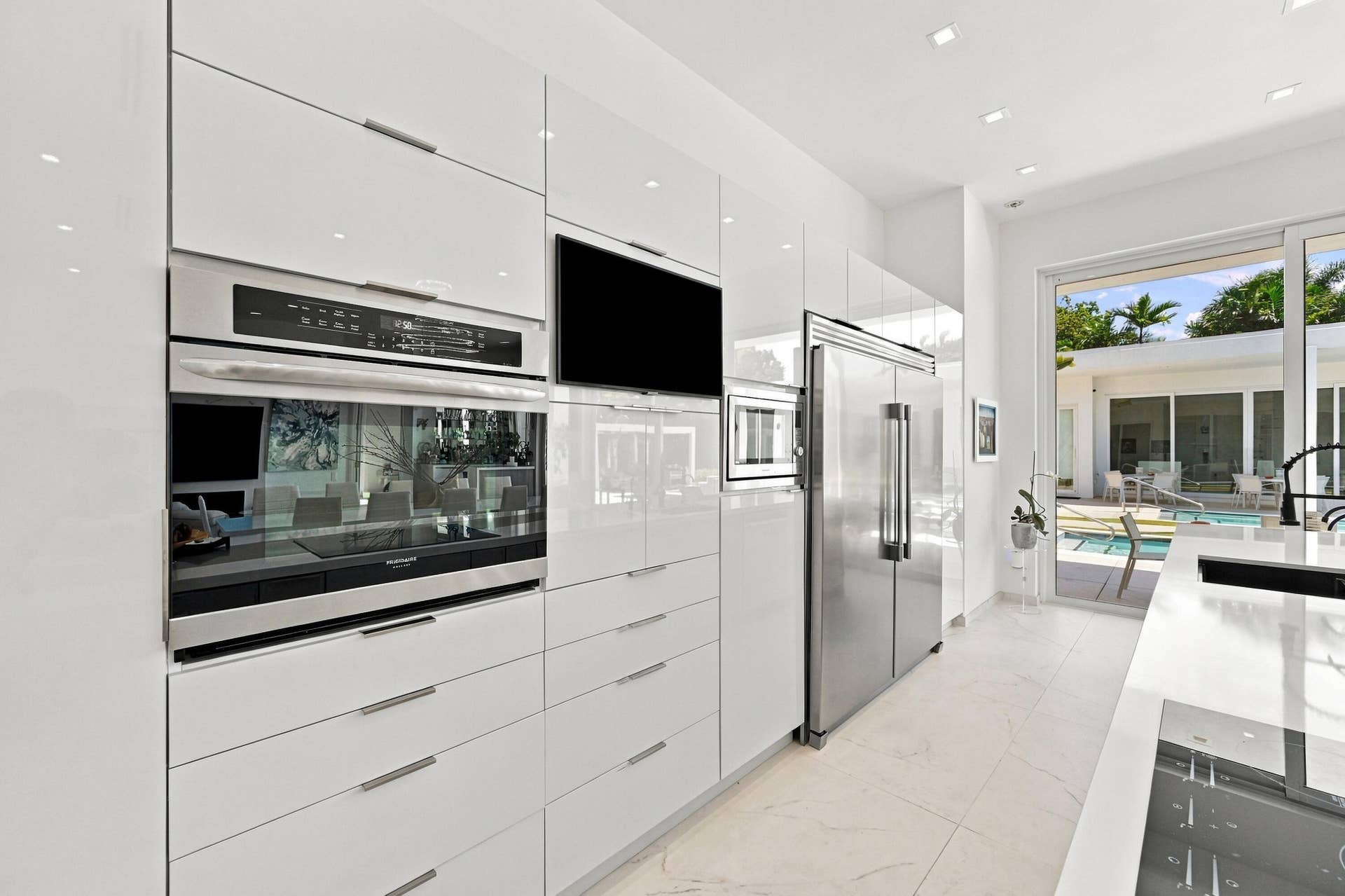 110 NE 16TH Place, Fort Lauderdale, FL 33305 Sleek kitchen featuring white high-gloss cabinetry, integrated stainless steel appliances, a built-in oven, and a large refrigerator