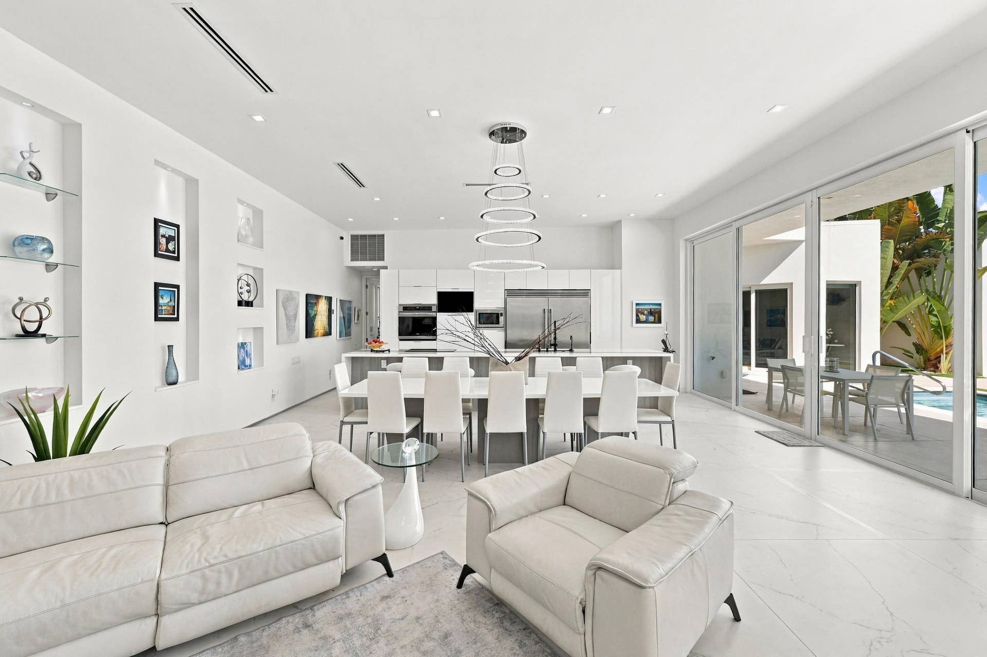 110 NE 16TH Place, Fort Lauderdale, FL 33305 Open-concept living space with white tile flooring, integrated kitchen with stainless steel appliances, modern ring chandelier, built-in wall niches, and large sliding glass doors