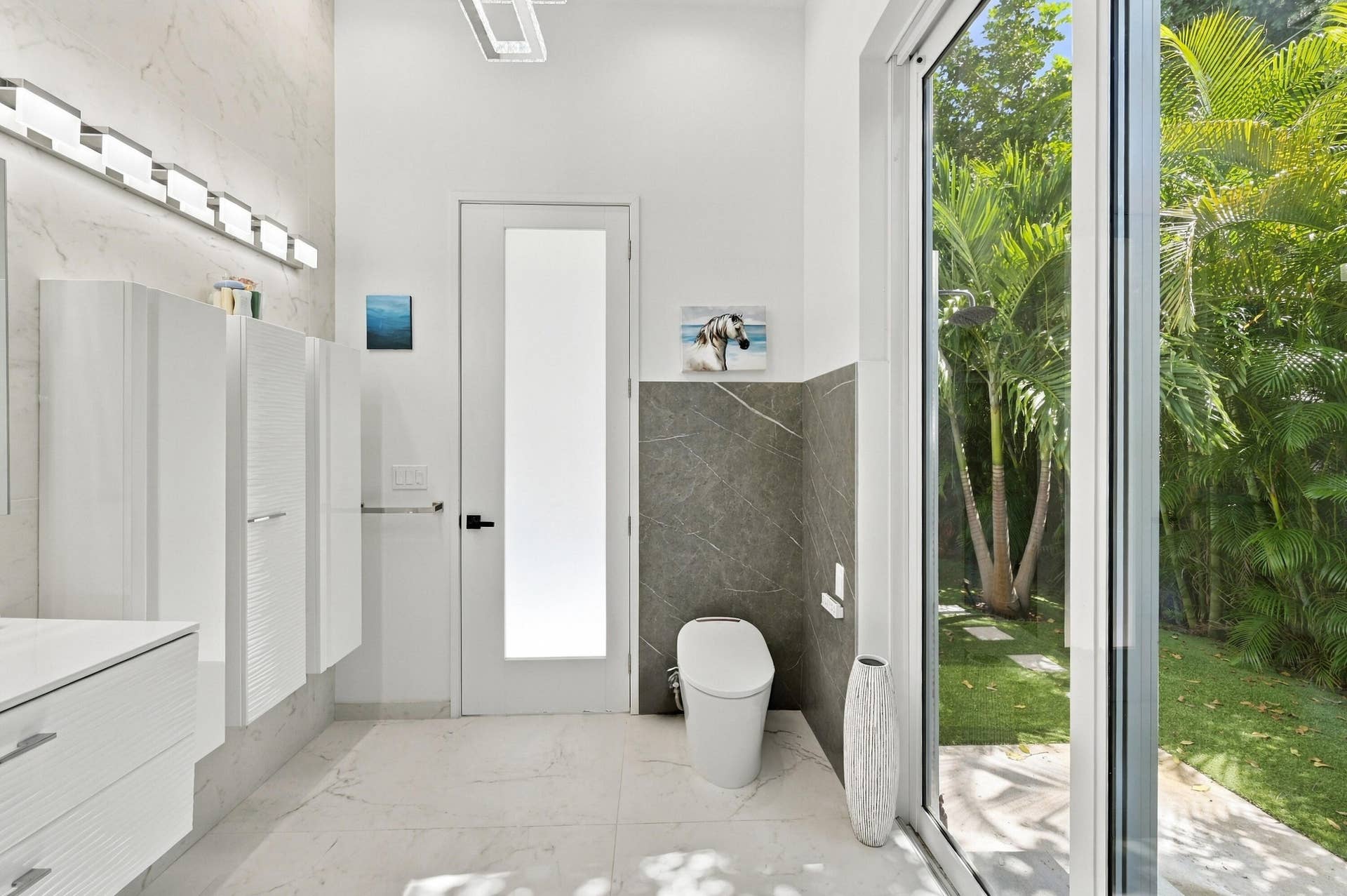 110 NE 16TH Place, Fort Lauderdale, FL 33305 Full-height glass panel door, large format tile flooring, modern wall-mounted toilet, full-height window, and contemporary vanity lighting